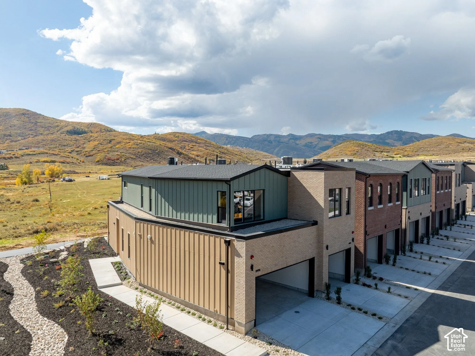 Multi-level exterior featuring a combination of brick and vertical metal siding, attached garages, and a mountainous backdrop