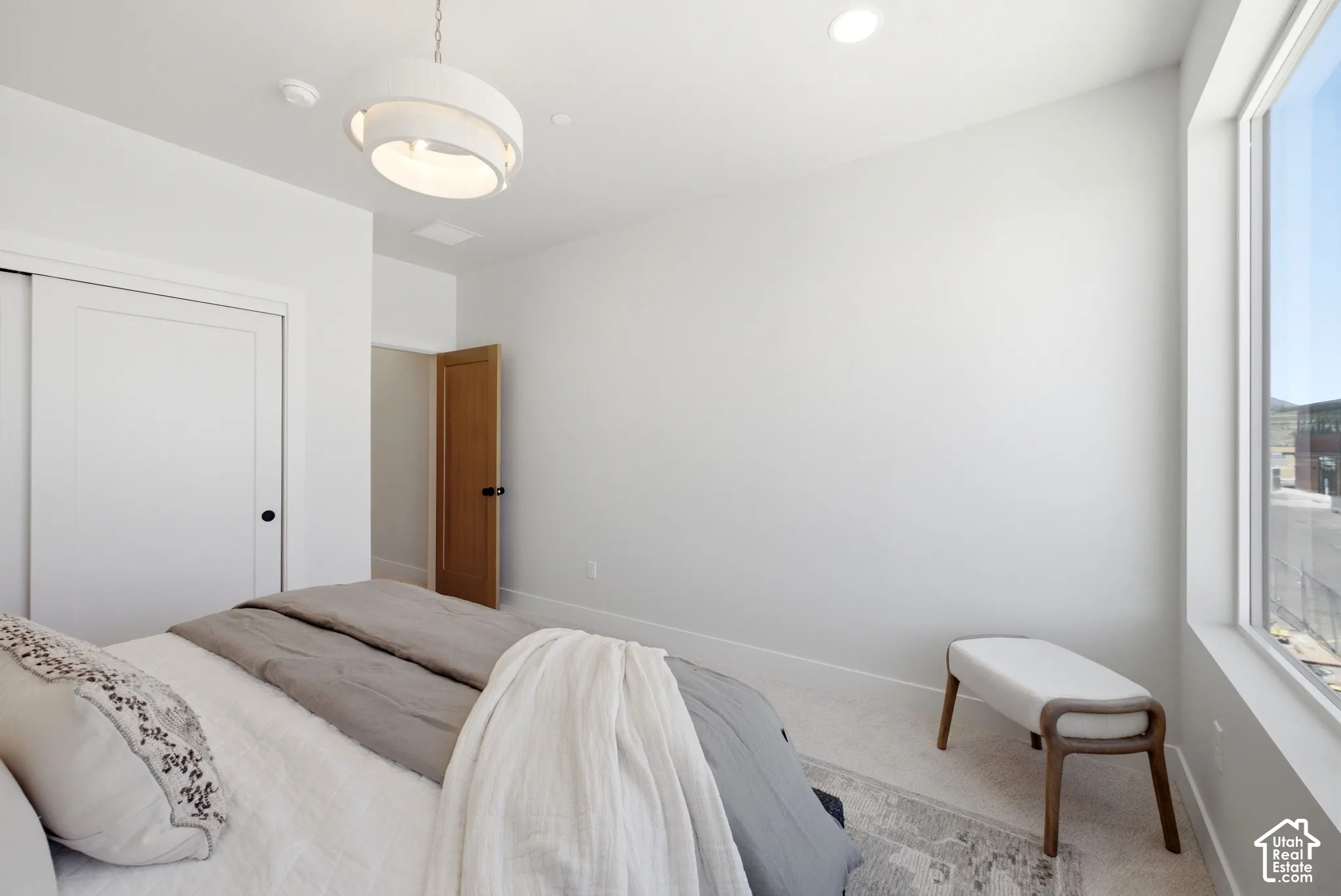Modern minimalist room featuring a large picture window, a contemporary multi-tiered pendant light fixture, recessed ceiling lighting, a wood-finish interior door, and a sliding-door closet