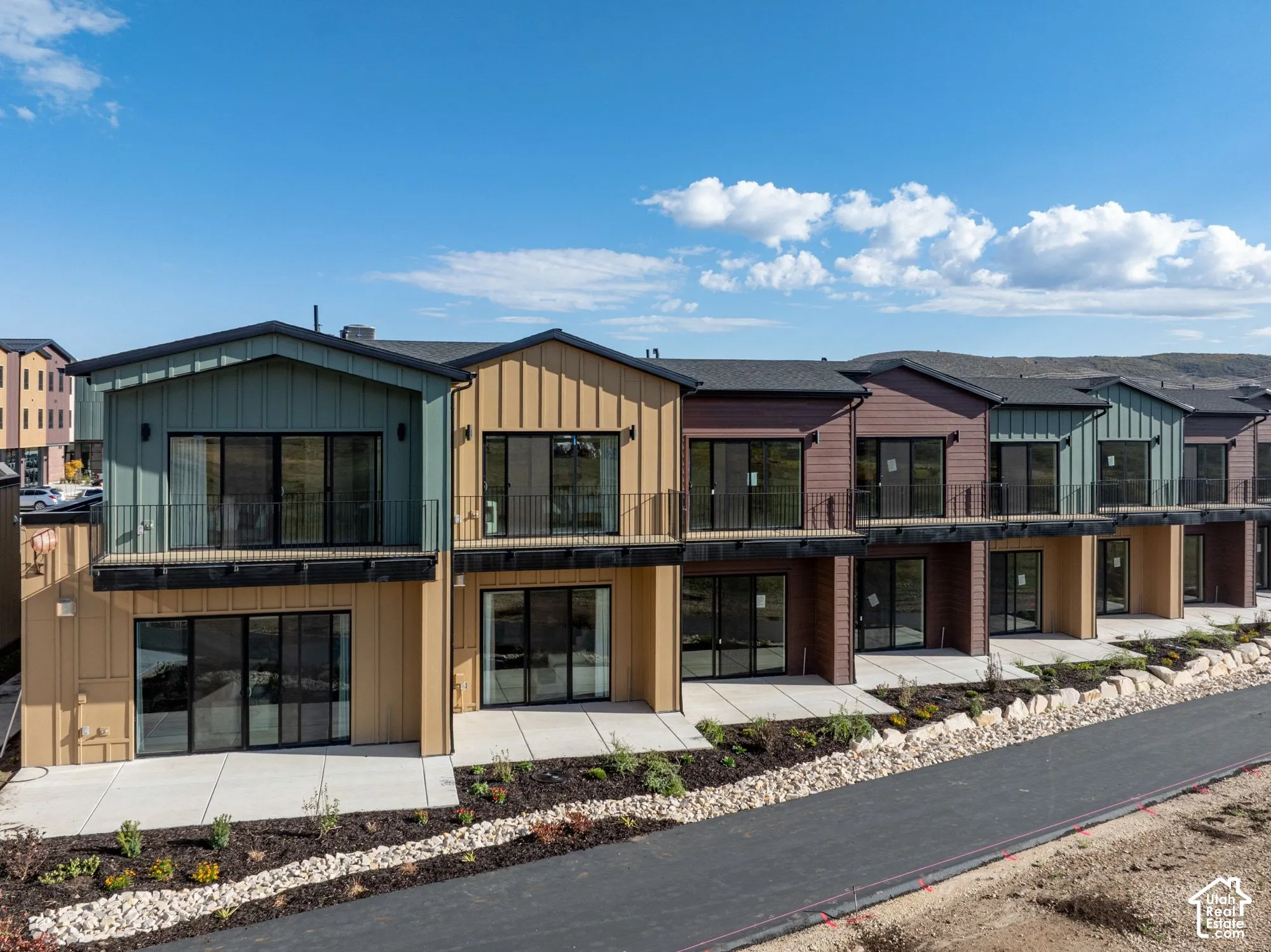 Multi-unit exterior featuring vertical board-and-batten siding, upper-level balconies with metal railings, sliding glass doors, and ground-level concrete patios