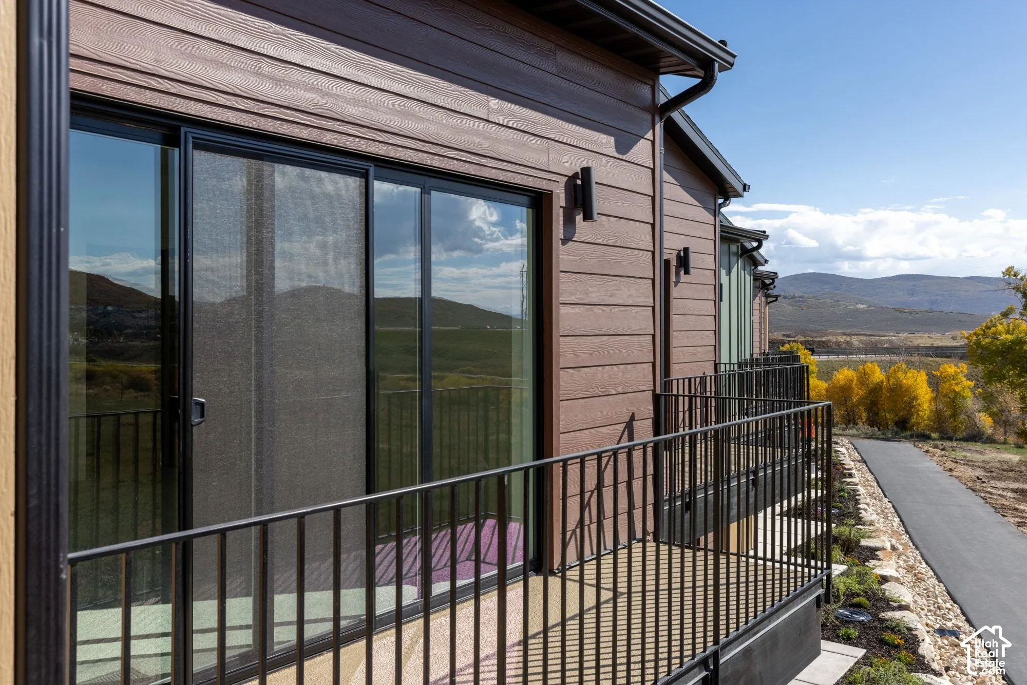 Exterior featuring horizontal siding, black metal railing, sliding glass doors, wall-mounted exterior lighting, and mountain scenery