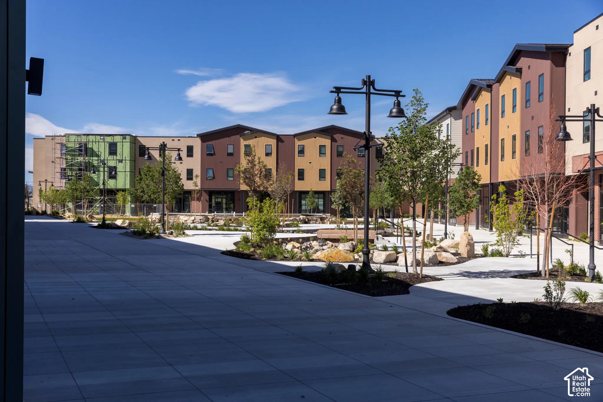 Multi-story residential complex featuring vertical siding, concrete pedestrian walkways, decorative street lamps, and landscaped rock gardens