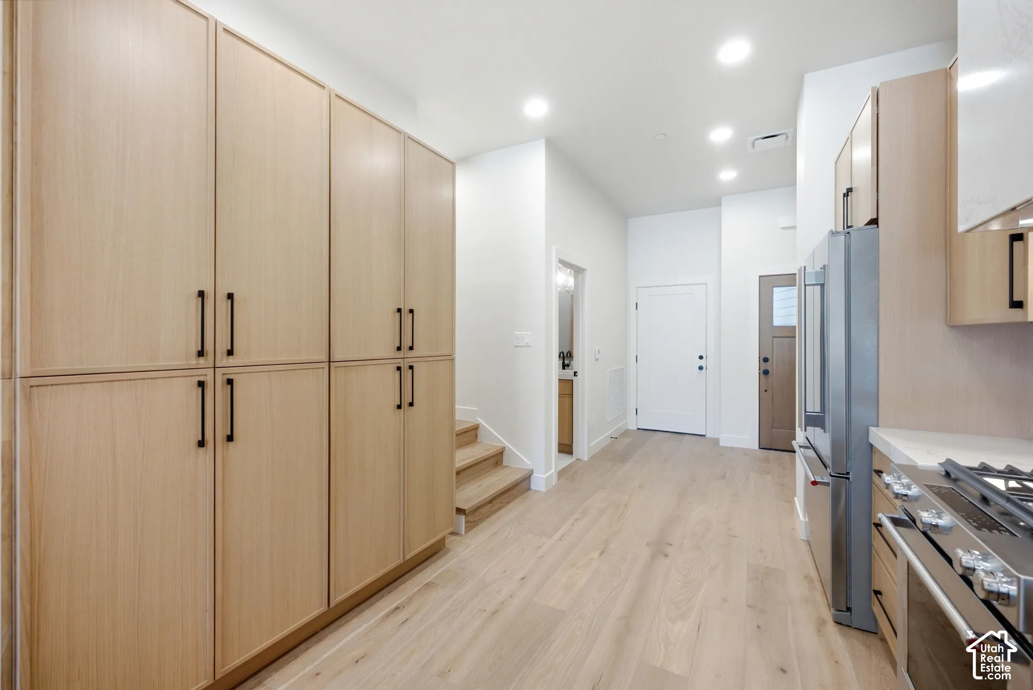 Full-height light wood cabinetry with matte black hardware, integrated stainless steel appliances, wood-finish flooring, and recessed ceiling lighting