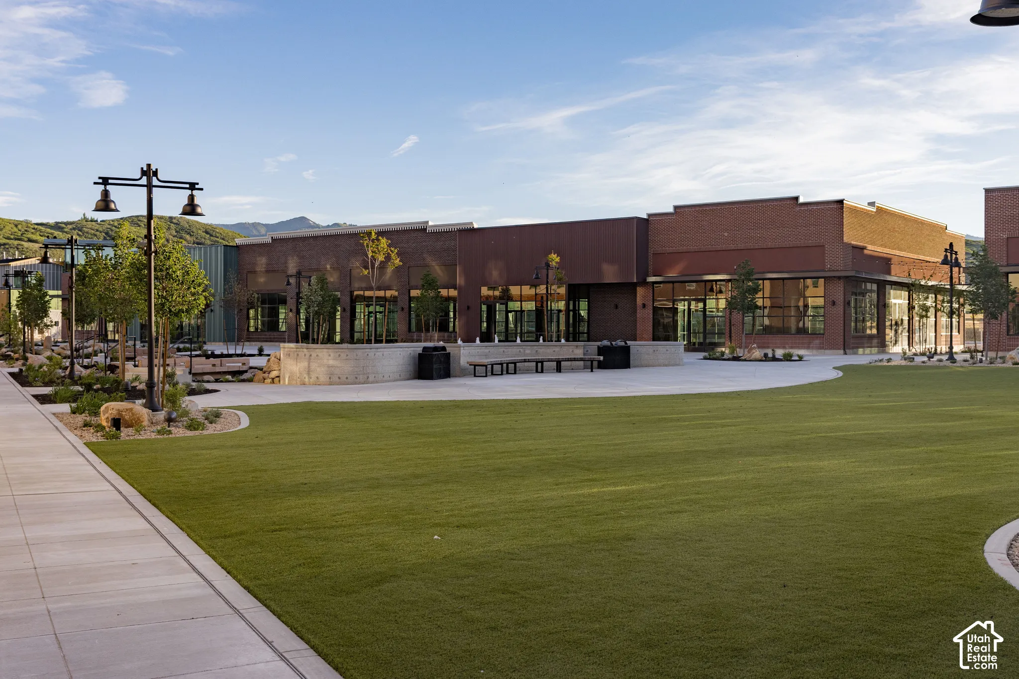 Expansive plaza featuring brick masonry construction, manicured synthetic turf, built-in concrete seating, and decorative metal light posts