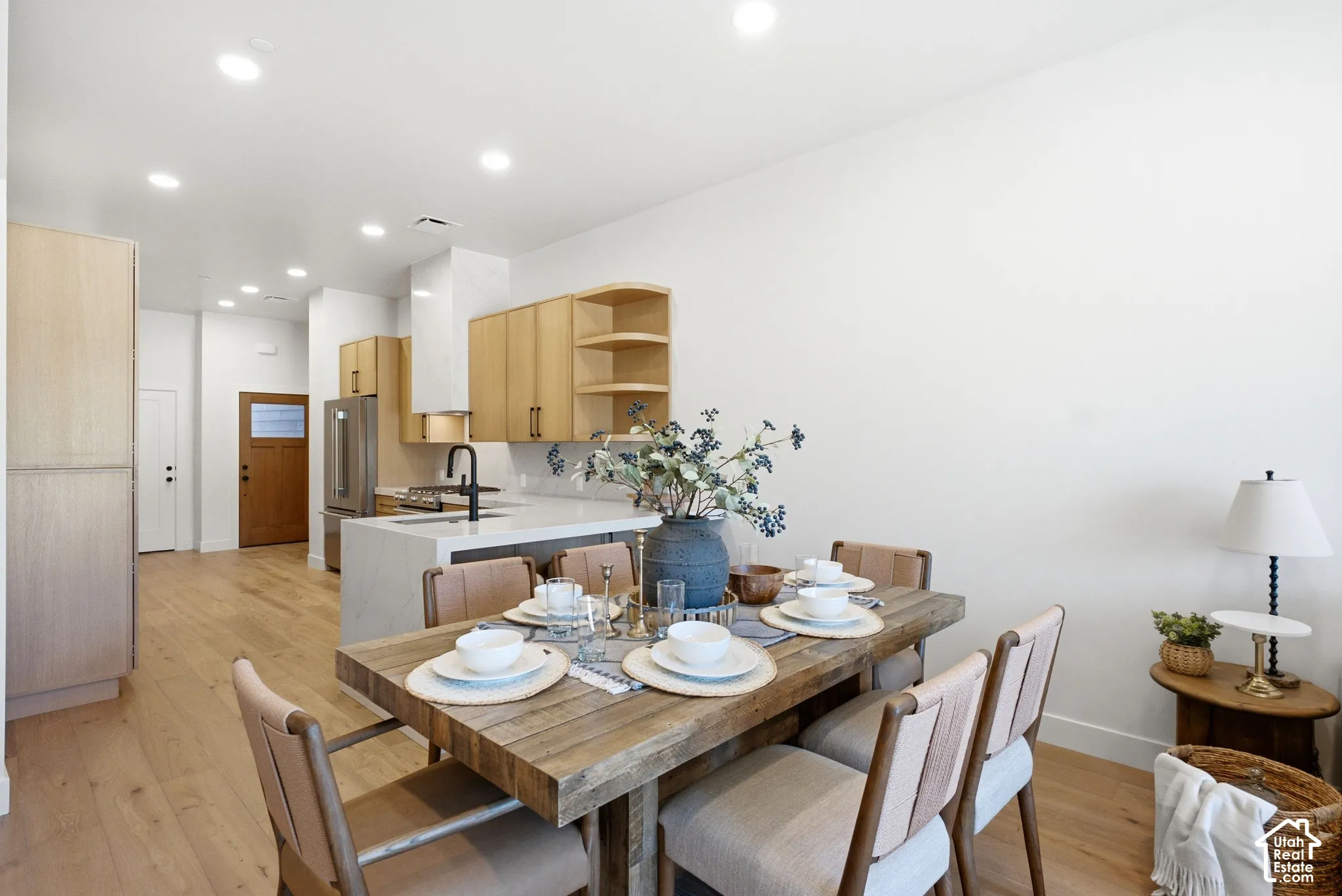 Light-tone wood-finish flooring, recessed lighting, flat-panel cabinetry, light-toned stone-surface countertops, and a waterfall-edge kitchen island