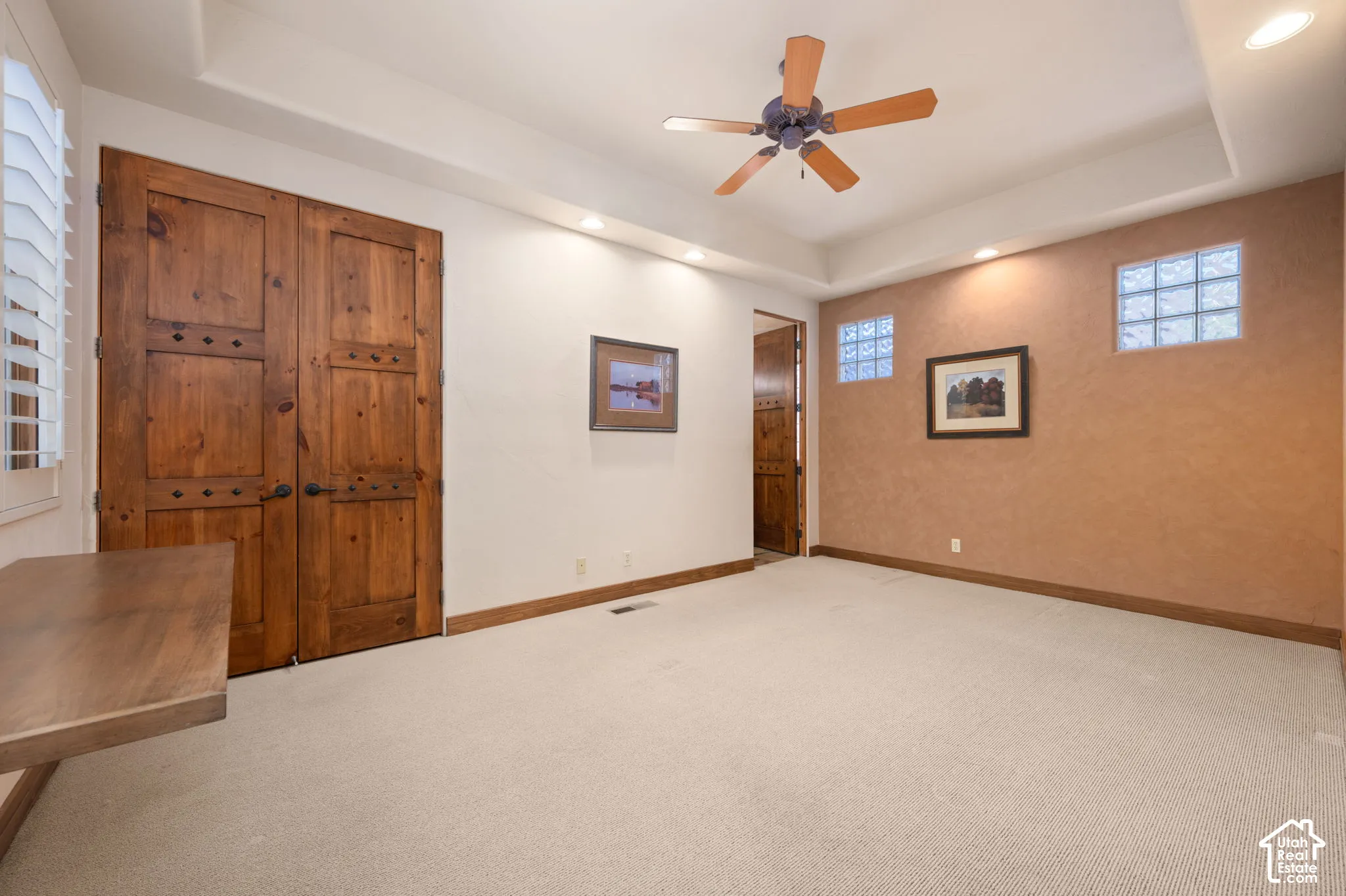 Room featuring a tray ceiling with recessed lighting, double stained-wood doors, glass block windows, and textured wall accents