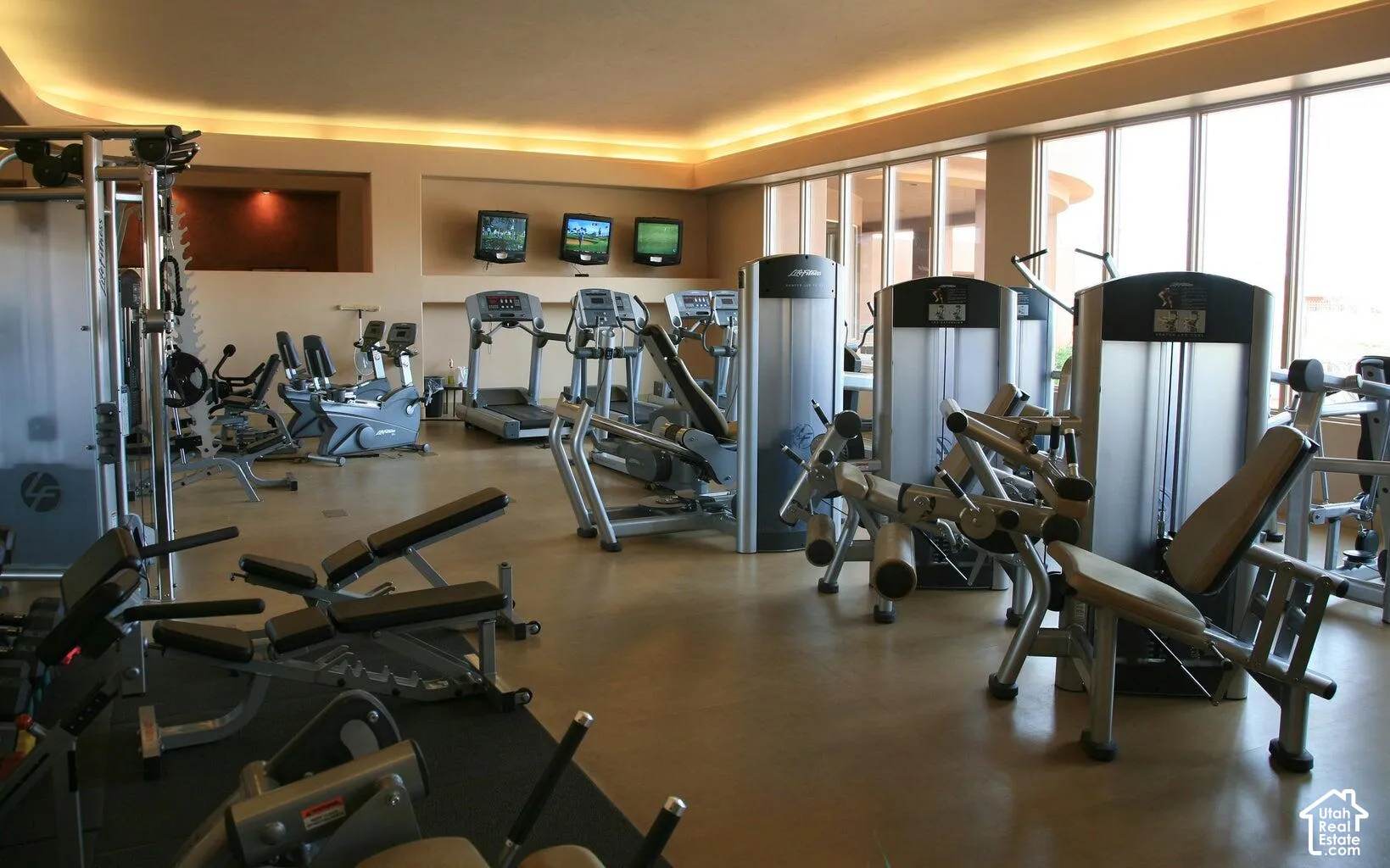 Fitness center featuring neutral flooring, recessed cove lighting, floor-to-ceiling windows, and wall-mounted television screens