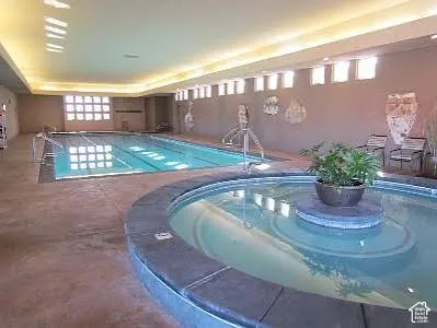 Indoor swimming area featuring a lap pool, a circular spa with a stone-finish coping, recessed perimeter ceiling lighting, and natural light via multiple rectangular windows