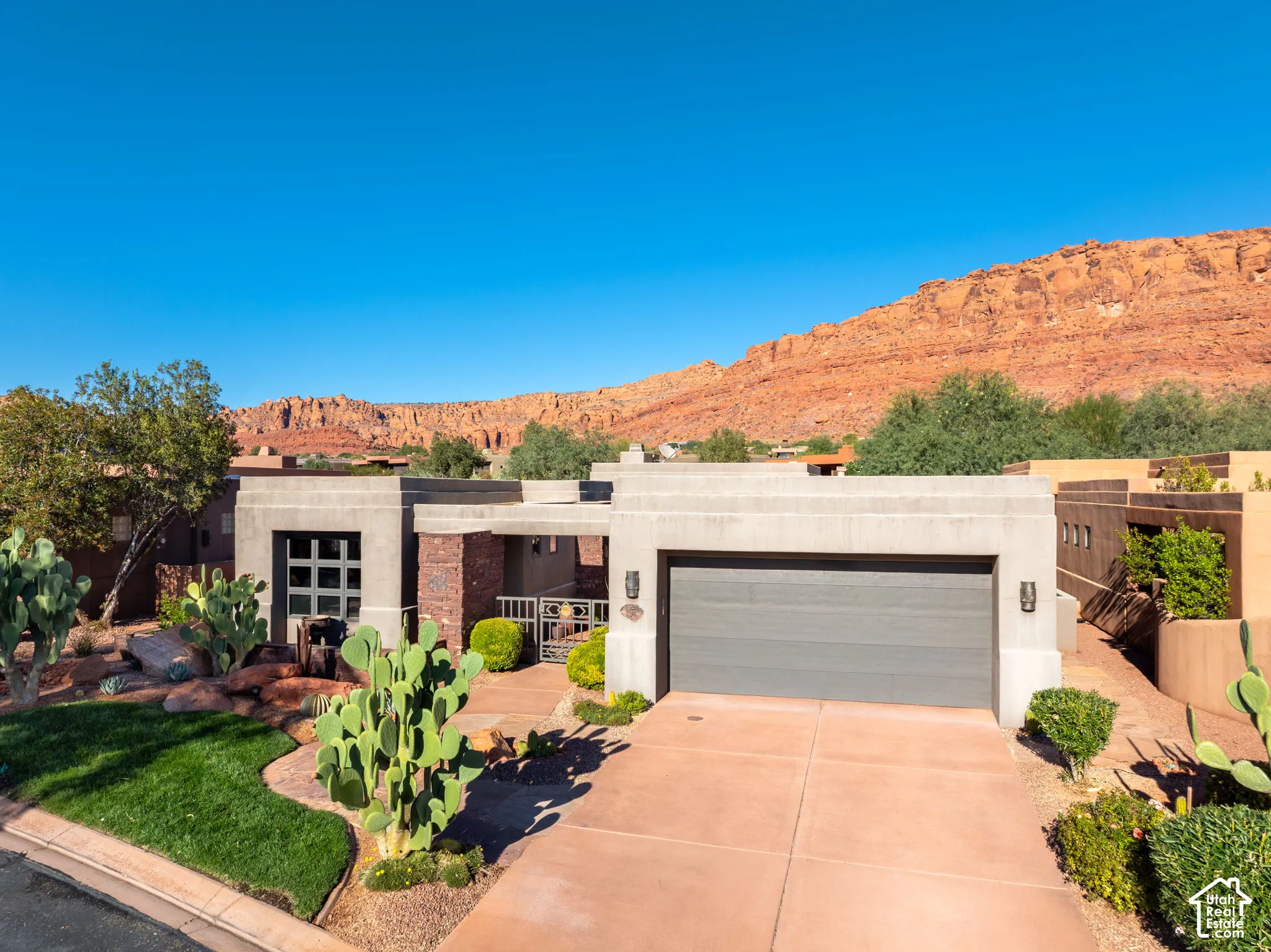 Contemporary exterior featuring a textured stucco facade, stone veneer accents, integrated garage, and xeriscaped front yard with a backdrop of red rock cliffs
