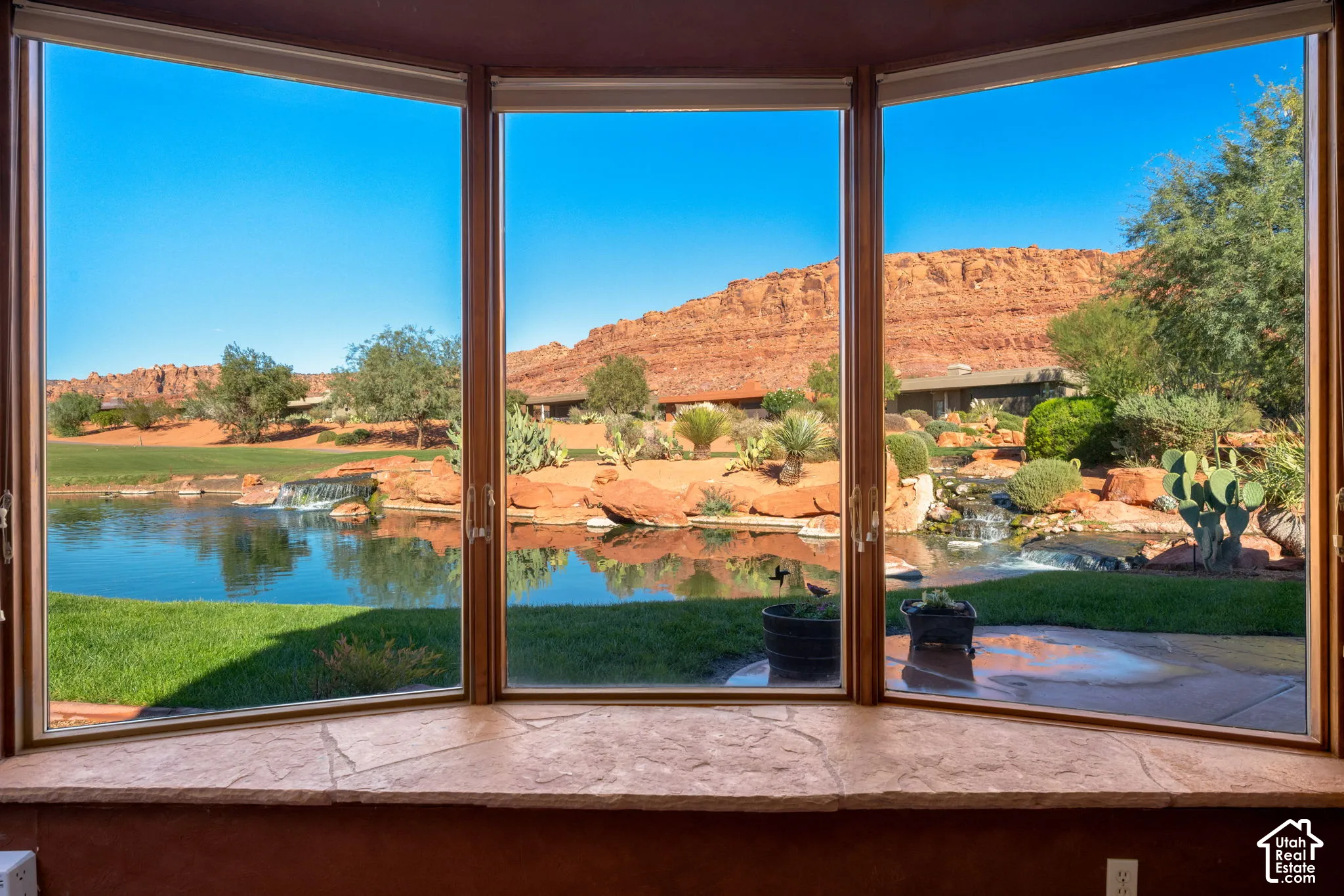 Expansive bay window featuring natural stone sill, large-pane glass, and scenic outdoor landscape including a pond, rock formations, and desert foliage