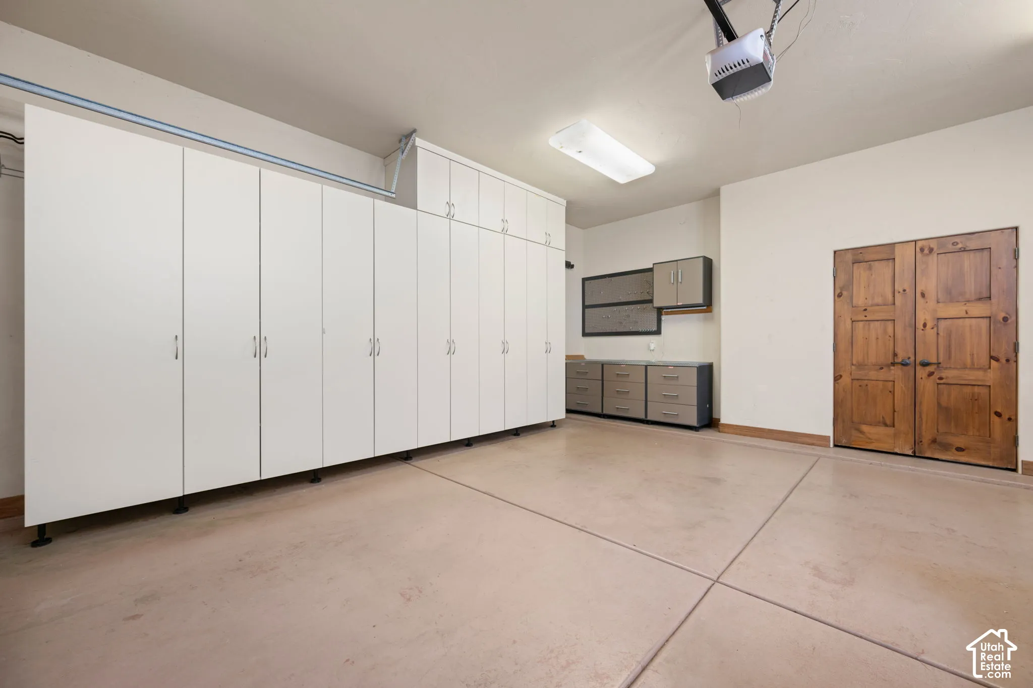 Garage featuring extensive white floor-to-ceiling cabinetry, separate wall-mounted storage units, a modular workstation, epoxy-coated flooring, and solid wood double doors