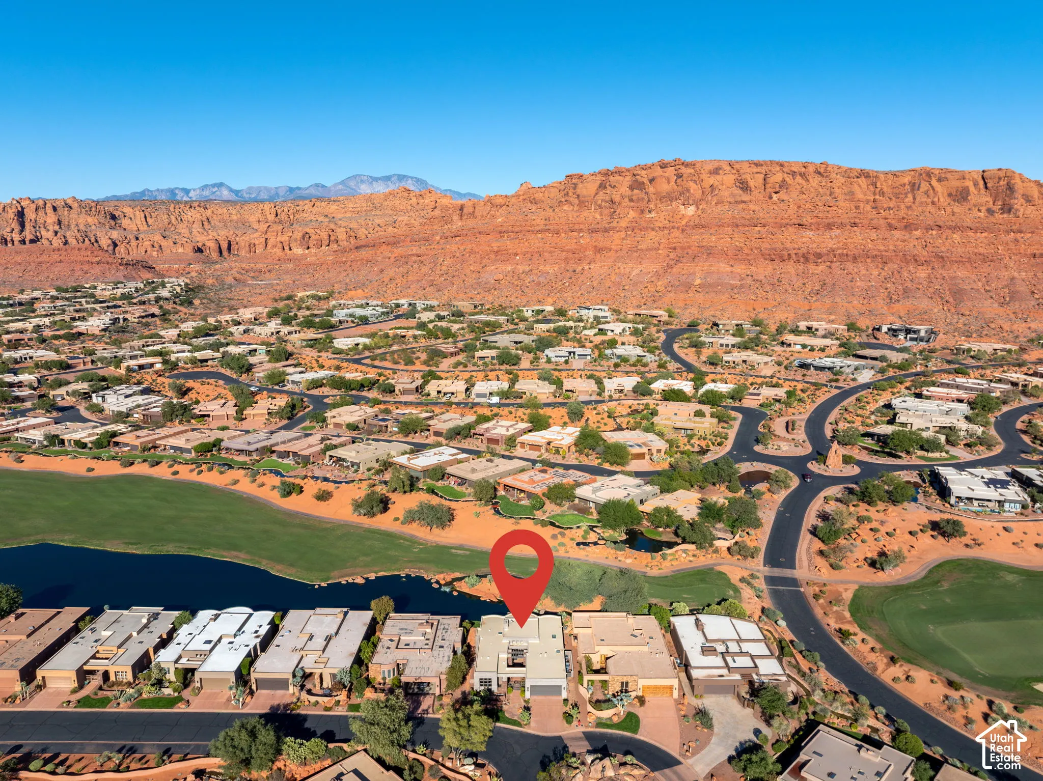 Aerial perspective featuring desert landscape, red rock mountain backdrop, and proximity to green space and water feature