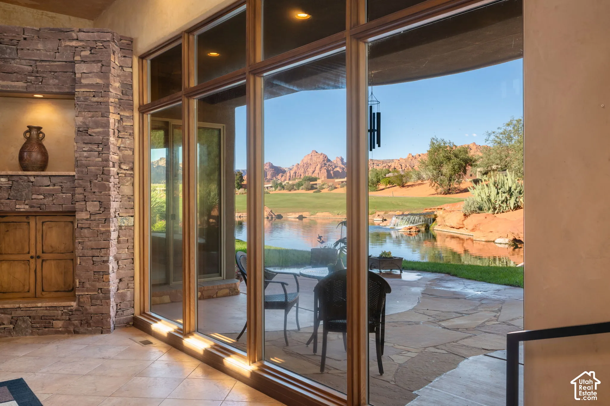 Floor-to-ceiling windows, stacked stone accent wall, custom built-in cabinetry with recessed lighting, tile flooring, and exterior flagstone patio