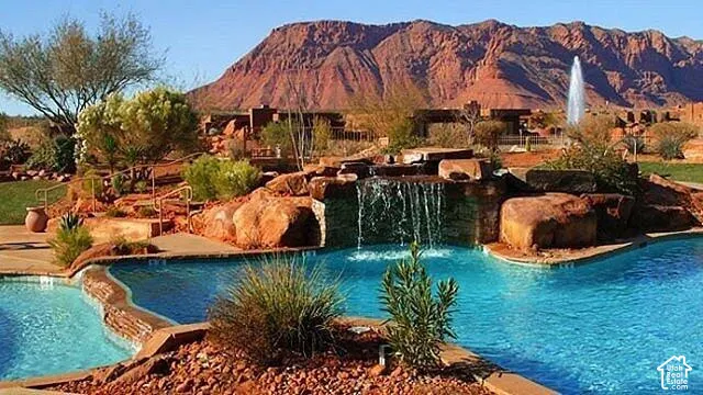 Swimming pool with integrated rock waterfall, natural stone hardscaping, water fountain, and desert landscaping set against a mountain backdrop