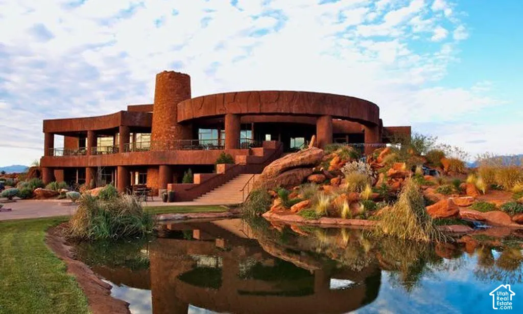 Custom-designed exterior featuring natural stone masonry, circular structural architecture, multi-level covered balconies with metal railings, a central stone tower, and a landscaped pond with surrounding rock formations