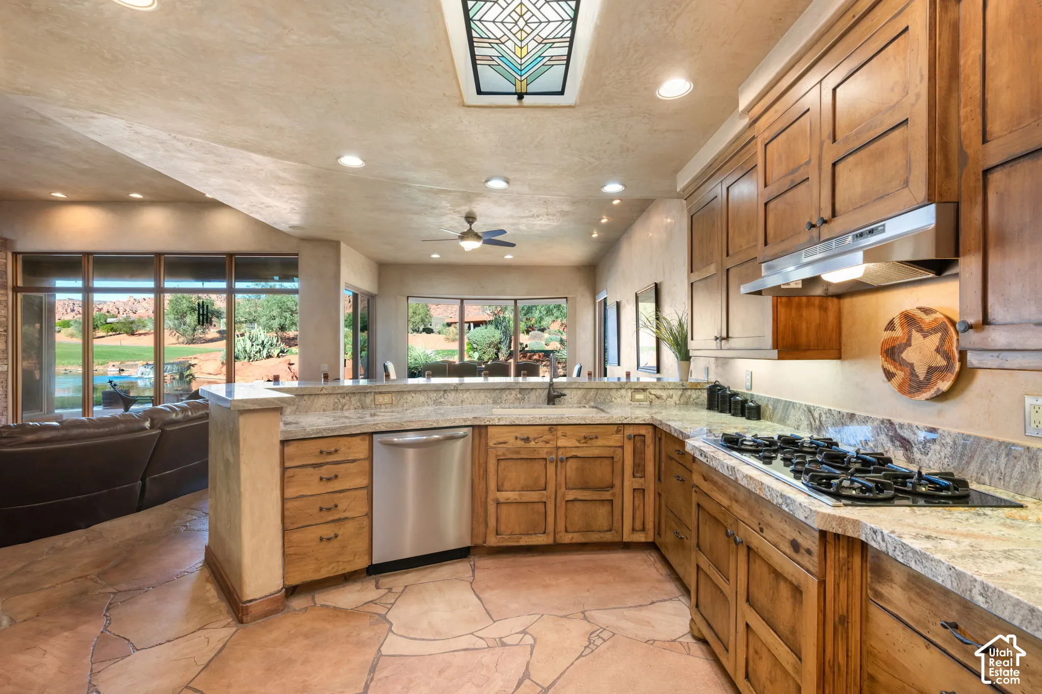 Kitchen featuring natural stone slab countertops, custom stained wood cabinetry, recessed lighting, a decorative stained-glass skylight, and stone flooring