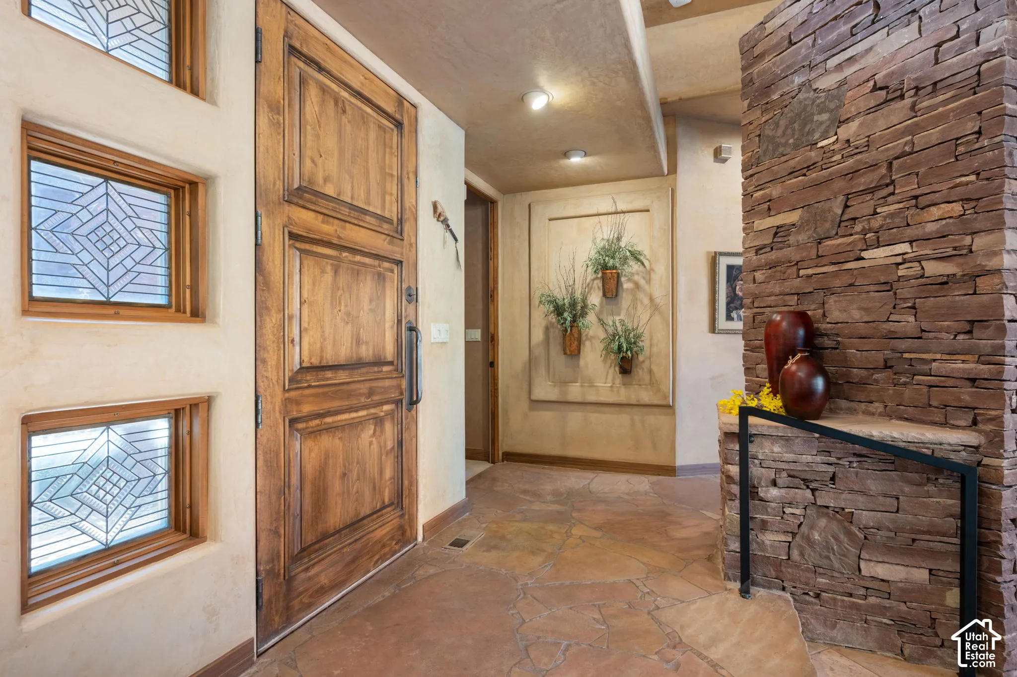 Entryway featuring a solid wood door, stacked stone accent pillar with integrated ledge, recessed ceiling lighting, textured wall finishes, and flagstone flooring