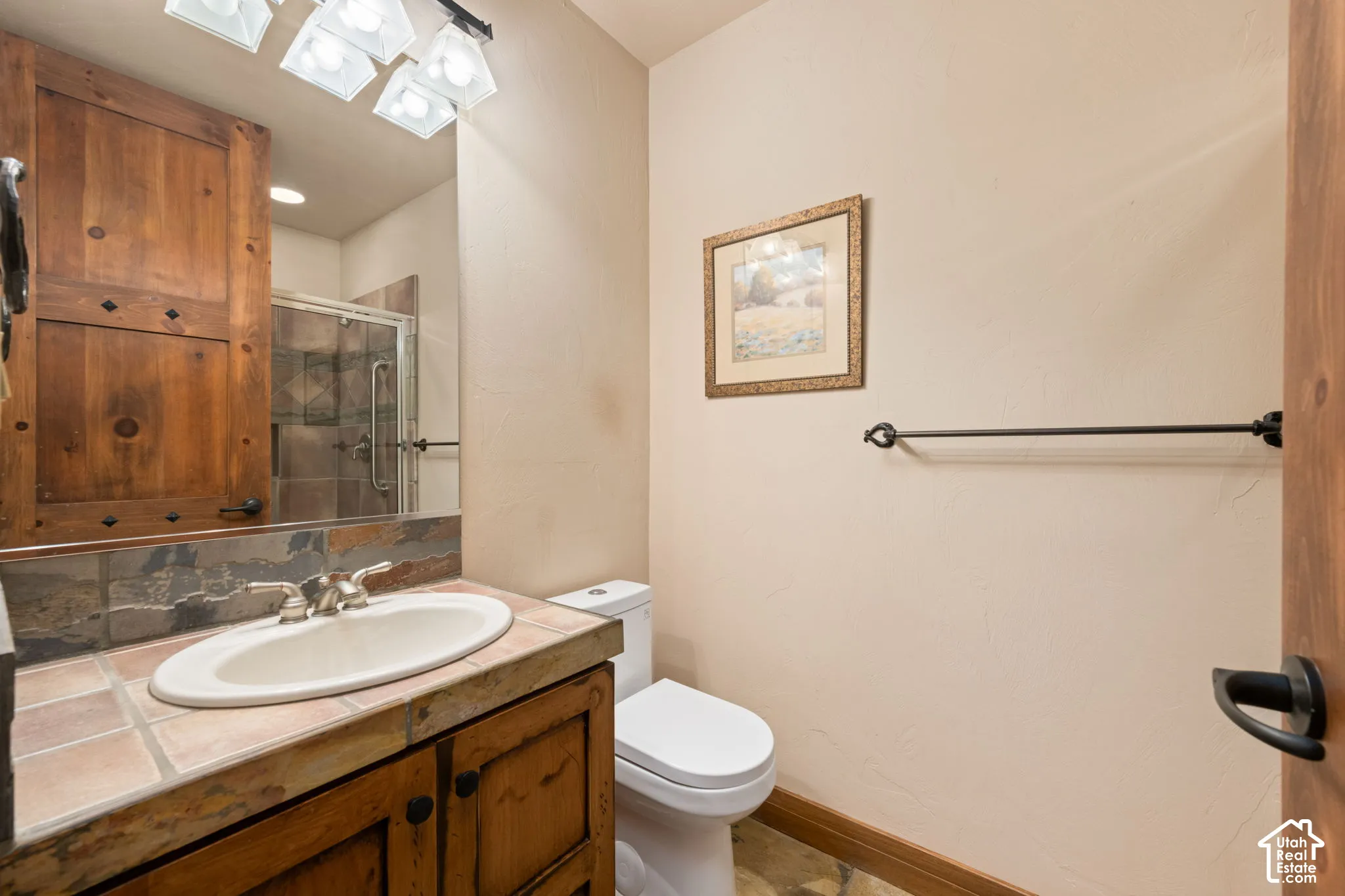 Custom wood cabinetry, stone tile countertop with integrated oval sink, multi-light fixture, and stone-finish backsplash