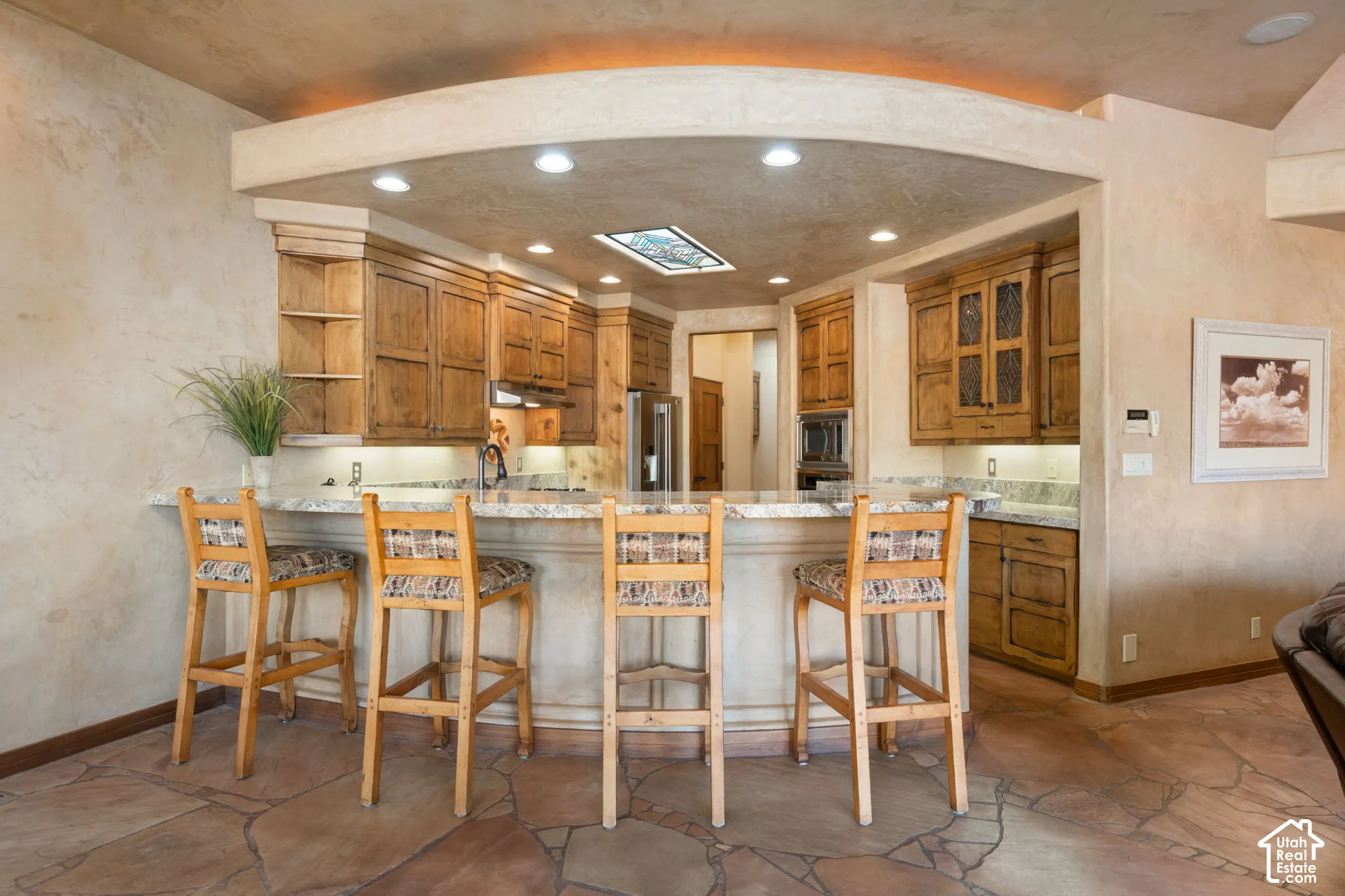 Kitchen featuring stone tile flooring, stained wood cabinetry, stone countertops, a recessed cove ceiling with integrated lighting, and a decorative ceiling inlay