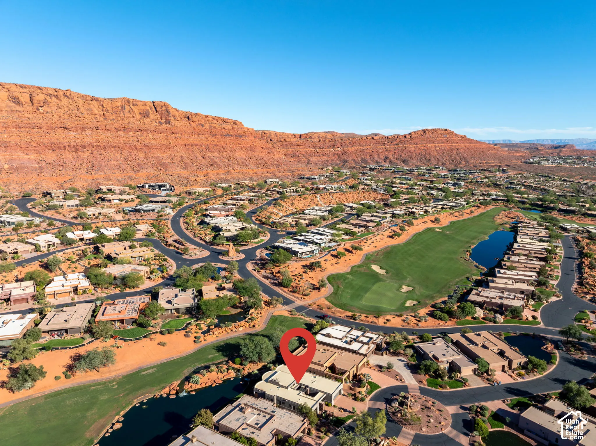 Aerial perspective of a property featuring red rock mountain backdrops, immediate golf course frontage, and a water feature