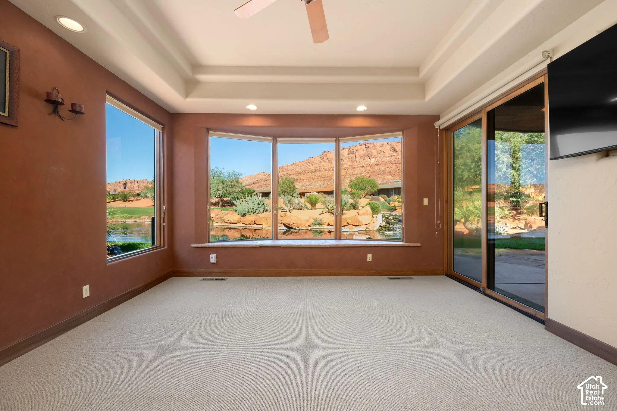 Tray ceiling, expansive bay window with built-in window seat, recessed lighting, and sliding glass doors featuring exterior rock formations and water feature scenery