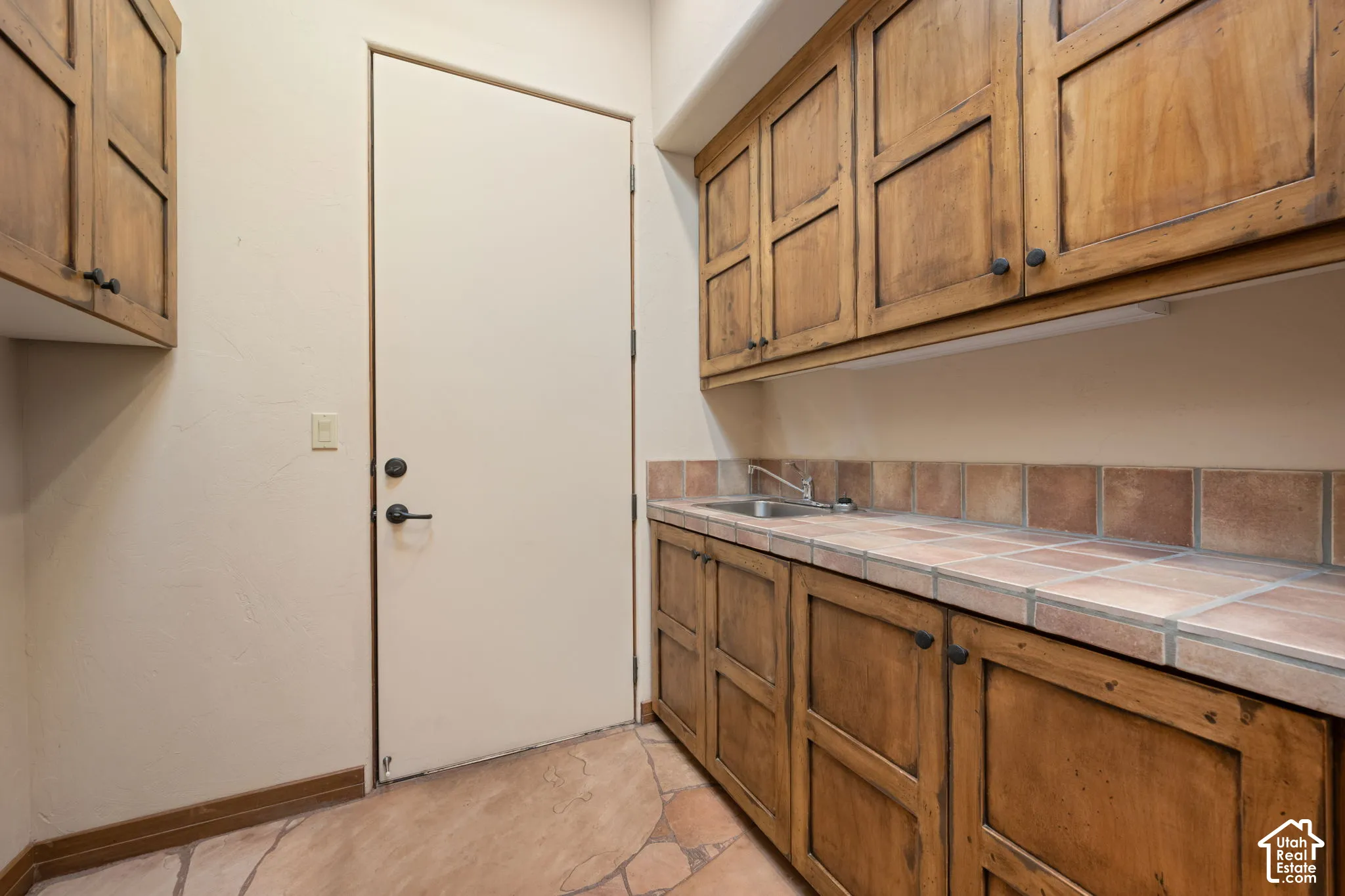 Utility space featuring custom wood cabinetry, tiled countertop, built-in sink, and stone-finish flooring