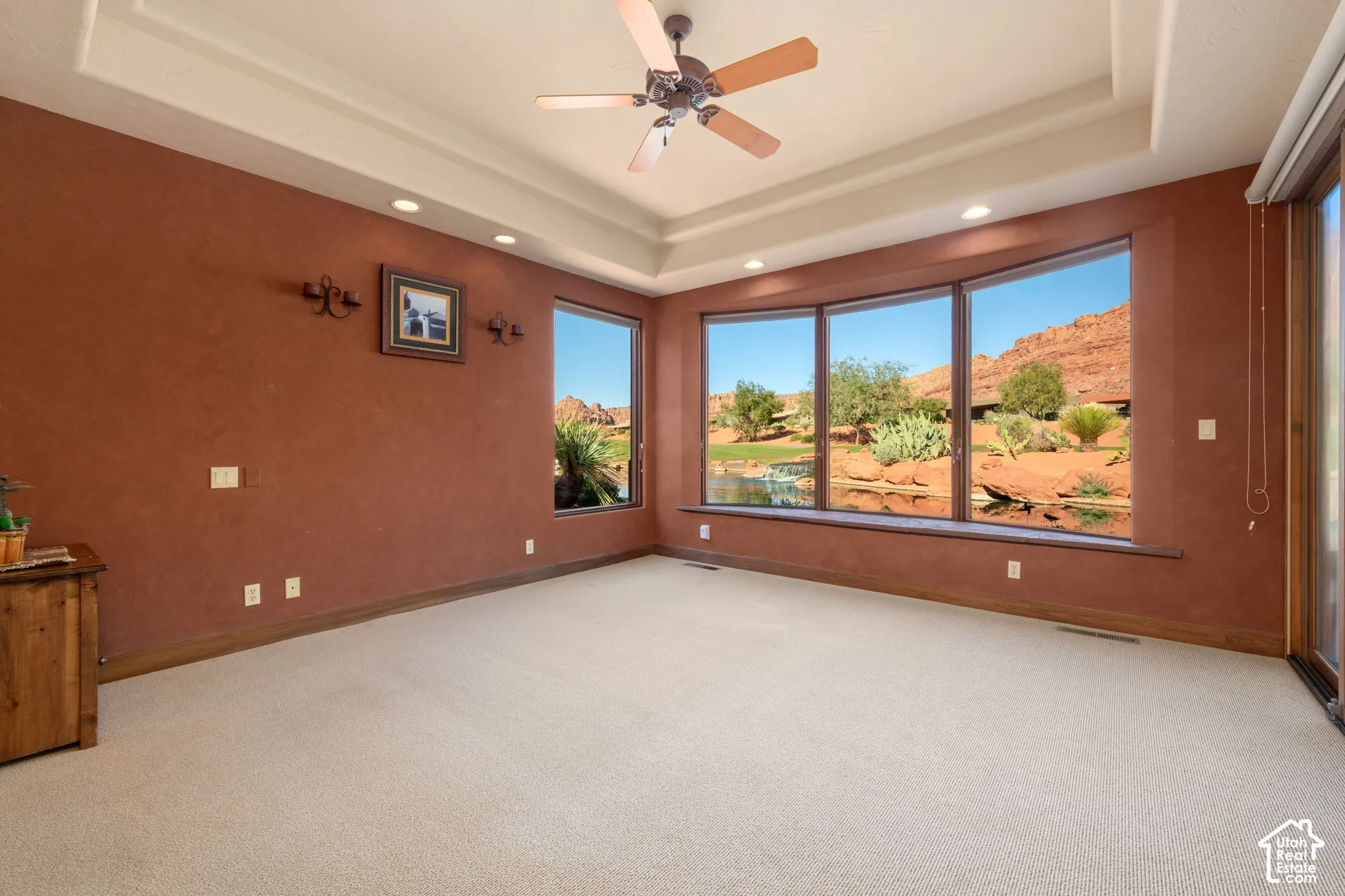 Tray ceiling with integrated recessed lighting, expansive bay windows, ceiling fan, and prominent red rock mountain backdrop