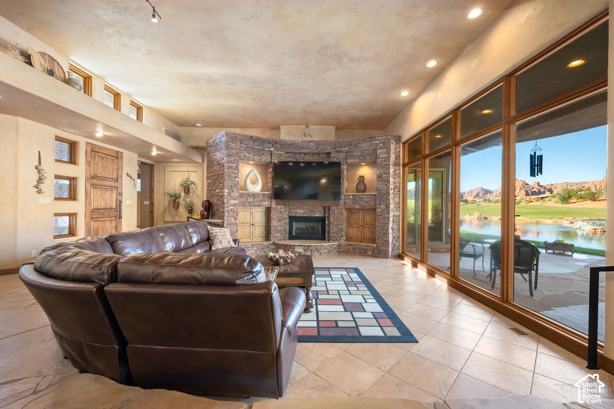 Living area featuring a curved stone fireplace surround with built-in cabinetry, floor-to-ceiling windows, tile flooring, and recessed lighting