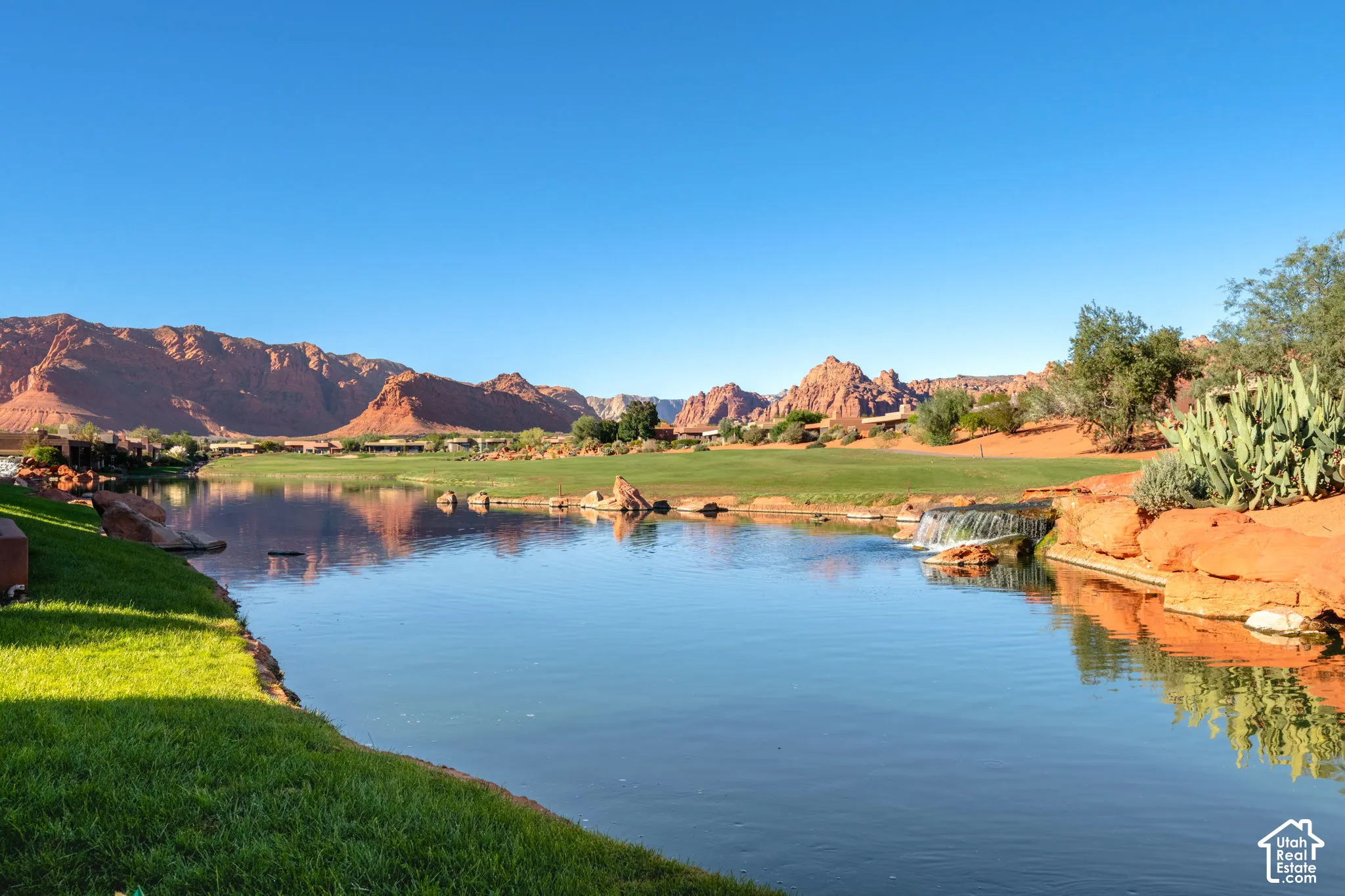 Water feature with rock edging, manicured lawn, red rock formations, and native landscaping