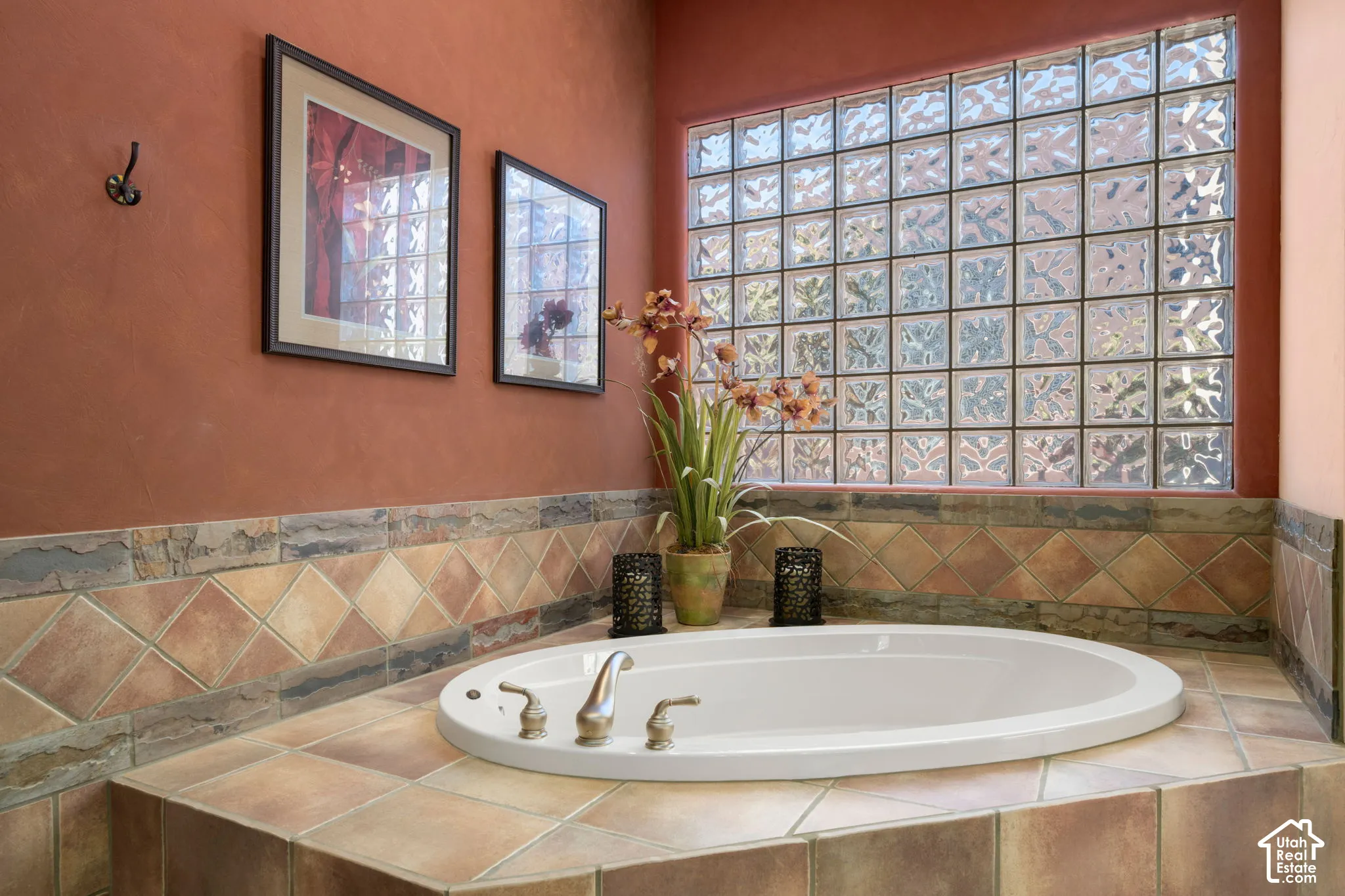 Oval soaking tub featuring a tile surround with diamond-patterned inlay, a large glass block window, and metallic finish plumbing fixtures