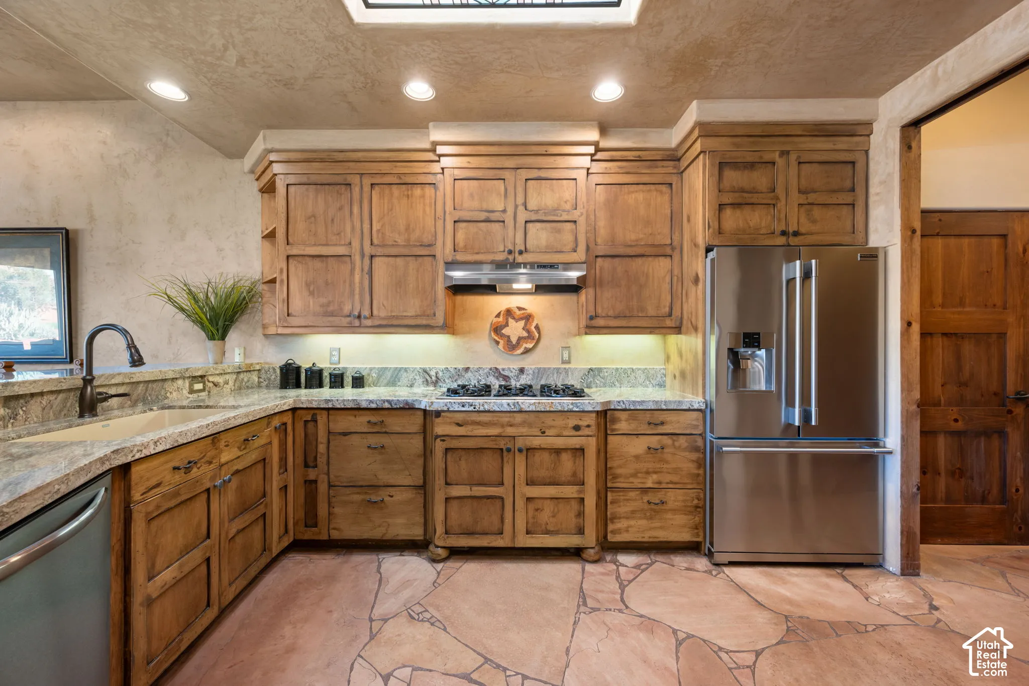 Kitchen featuring custom wood cabinetry, natural stone countertops, a stainless steel gas cooktop, recessed lighting, and flagstone flooring