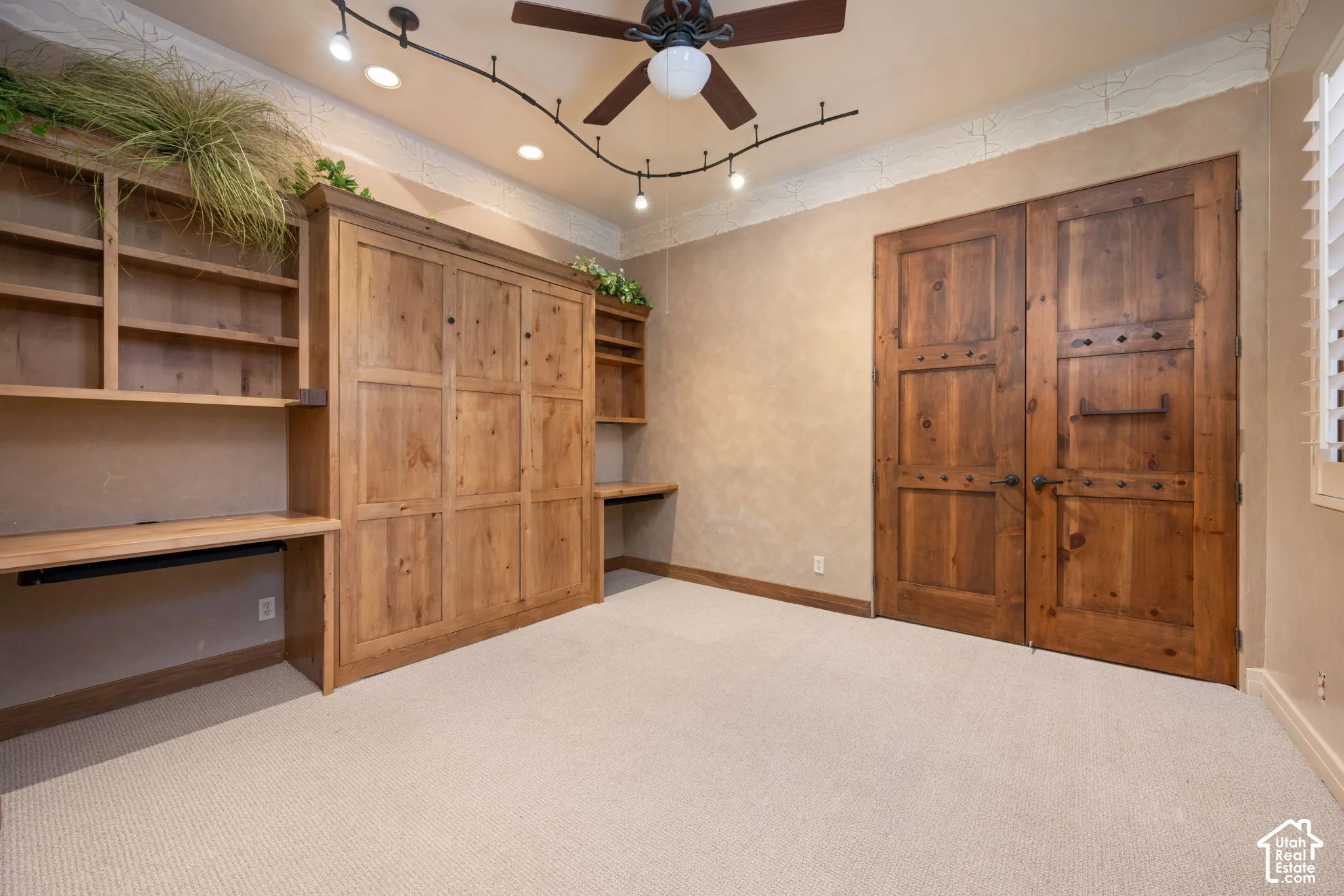 Custom wood cabinetry featuring built-in desks, decorative double wood doors, ceiling-mounted track lighting, and a ceiling fan