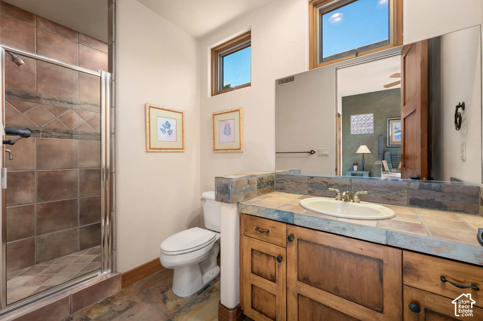 Bathroom featuring a walk-in shower with tile surround, wood cabinetry, tile countertops, an integrated basin, and large wall-mounted mirror