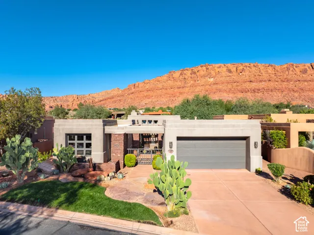 Single-story stucco exterior featuring a stone-accented facade, decorative metal courtyard gate, multi-panel garage door, and a backdrop of red rock cliffs