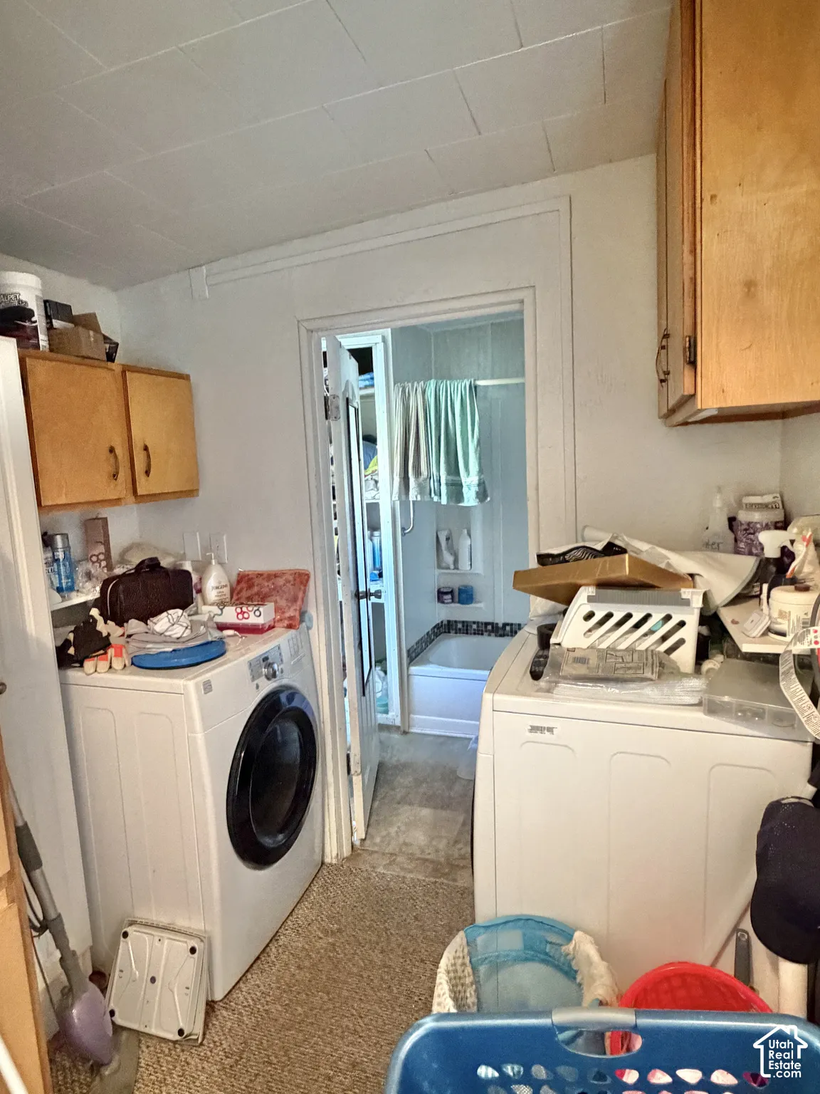 Laundry area featuring wood cabinetry and an entryway to a space containing a shower-tub combination with a tile surround