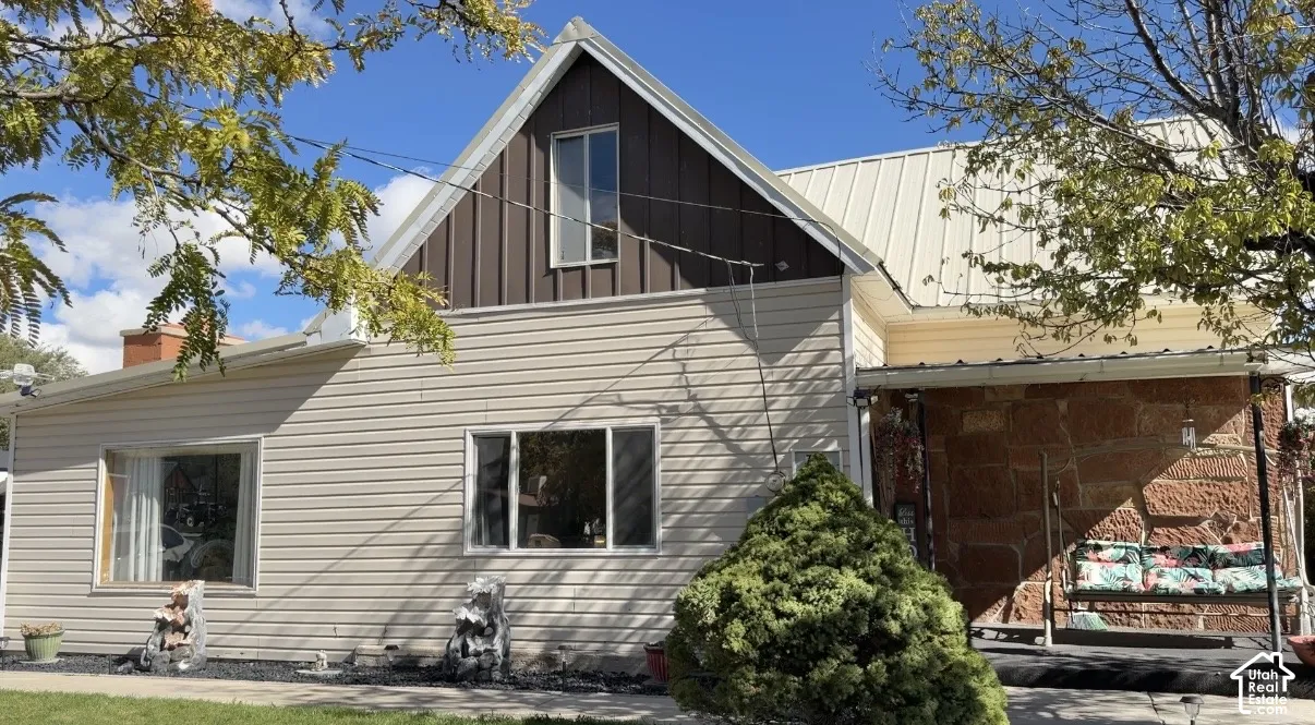 Exterior featuring horizontal vinyl siding, vertical metal gable siding, metal roofing, and natural stone masonry accents on a covered porch