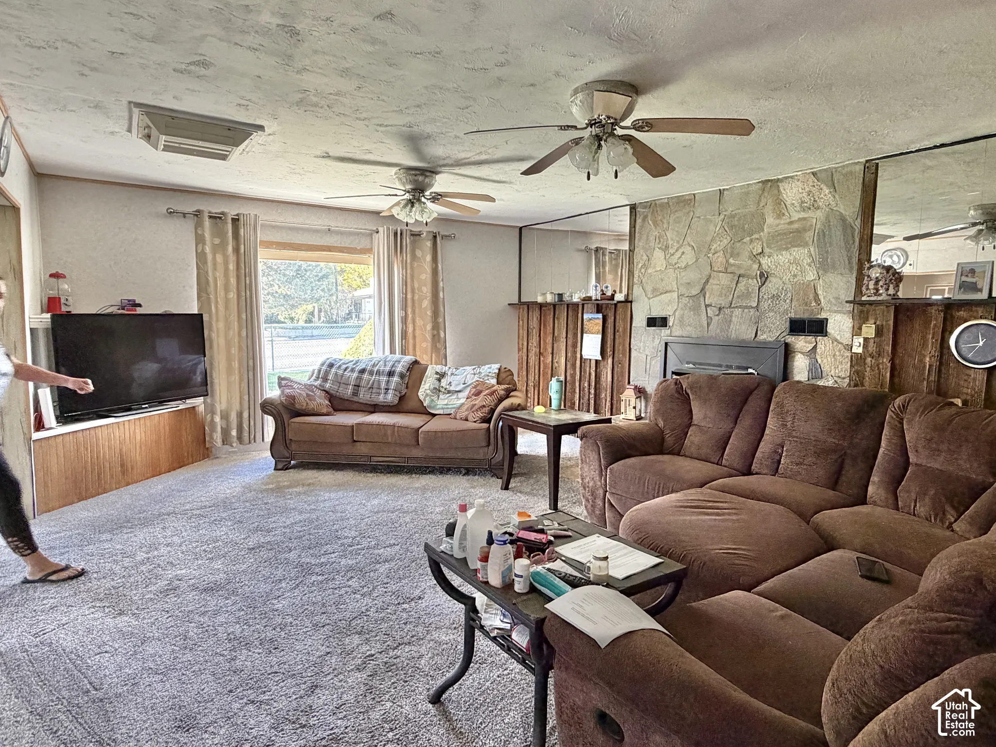 Living area featuring a floor-to-ceiling natural stone fireplace, wood-paneled accents, mirrored walls, and dual ceiling fans