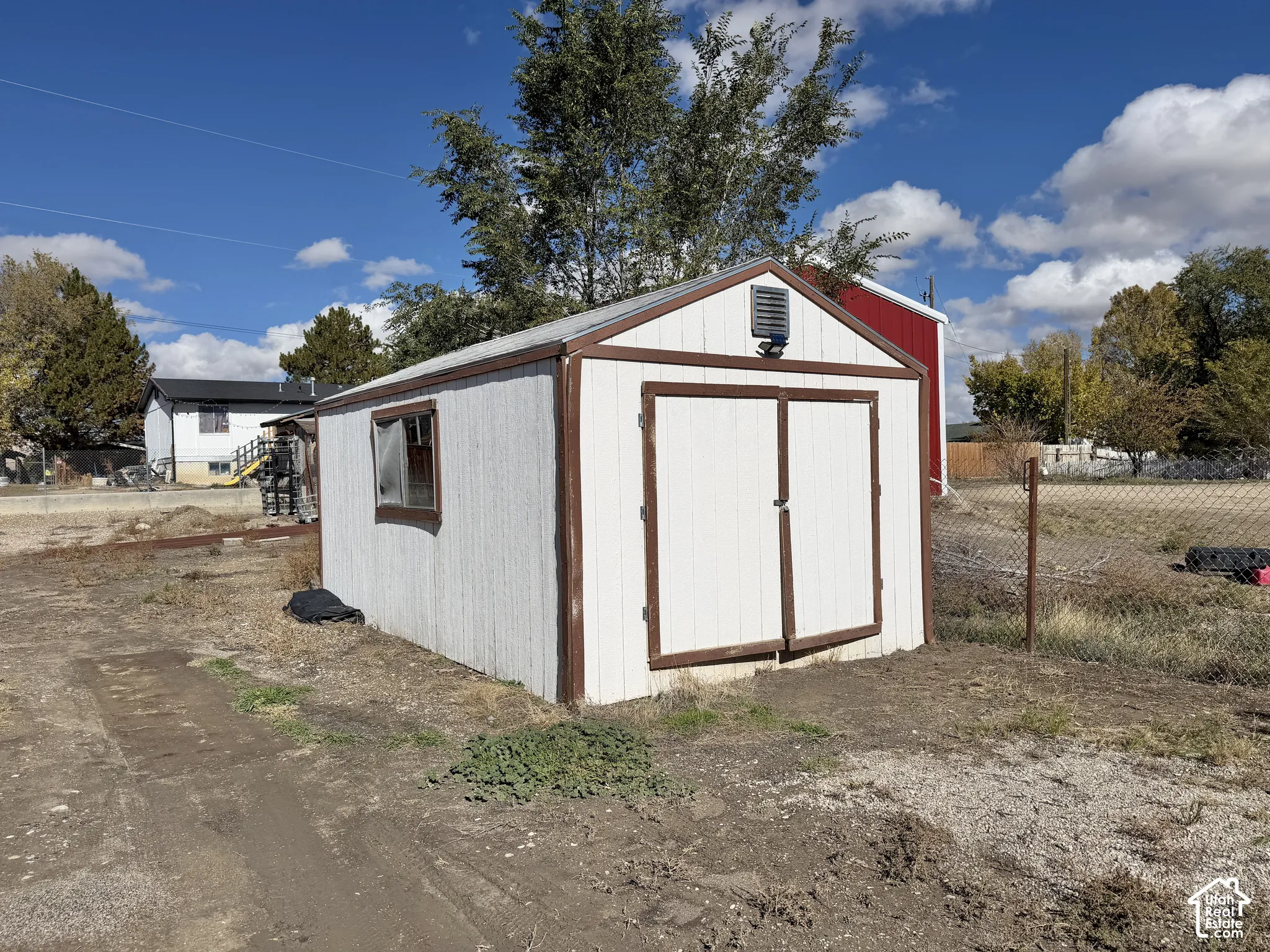 Detached storage structure with white panel siding, brown trim, double-door entry, a gable roof, and a side-mounted window