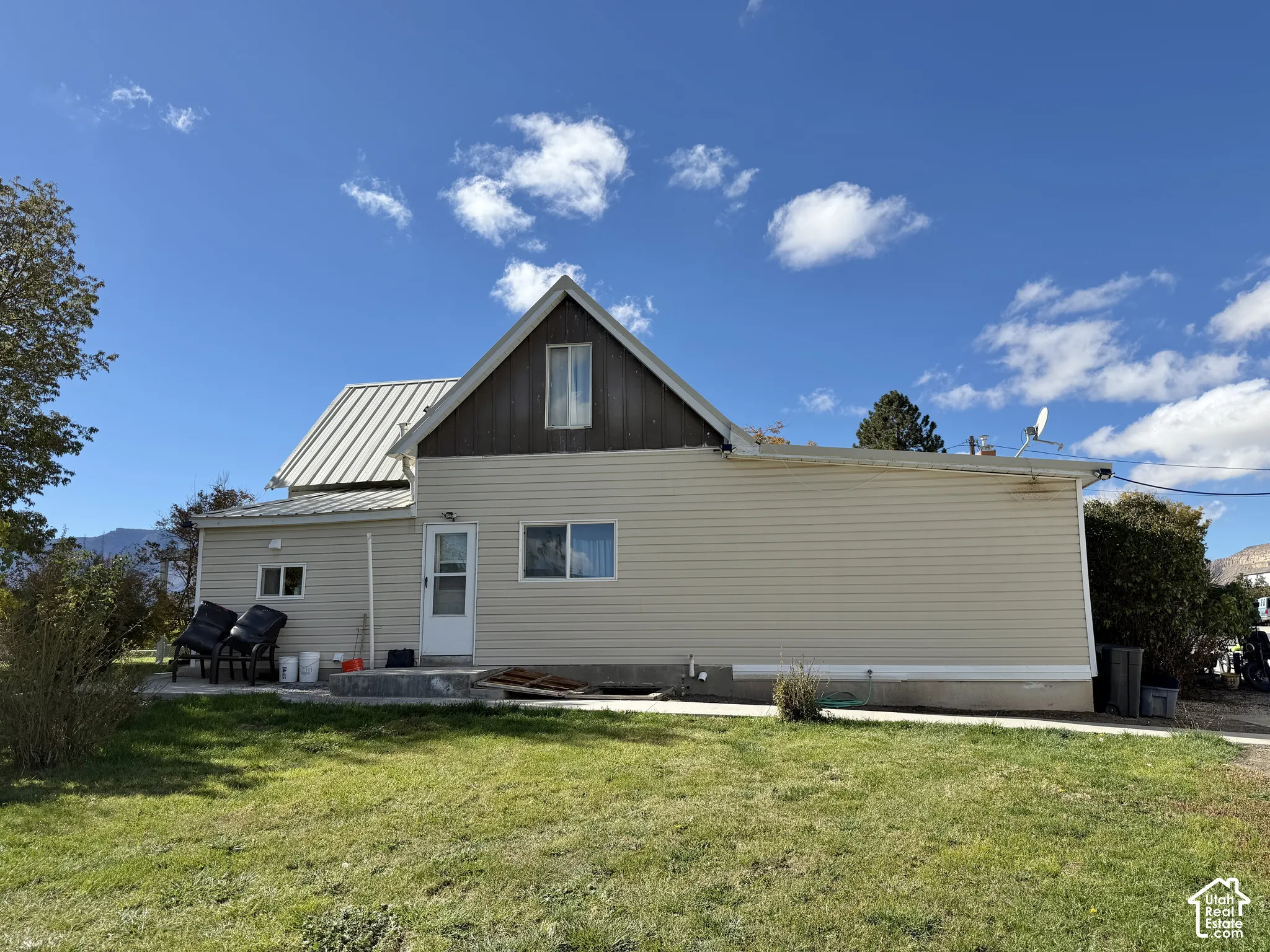 Exterior featuring light-colored horizontal siding, vertical dark wood-finish accents on the gable, a metal roof, and a concrete patio