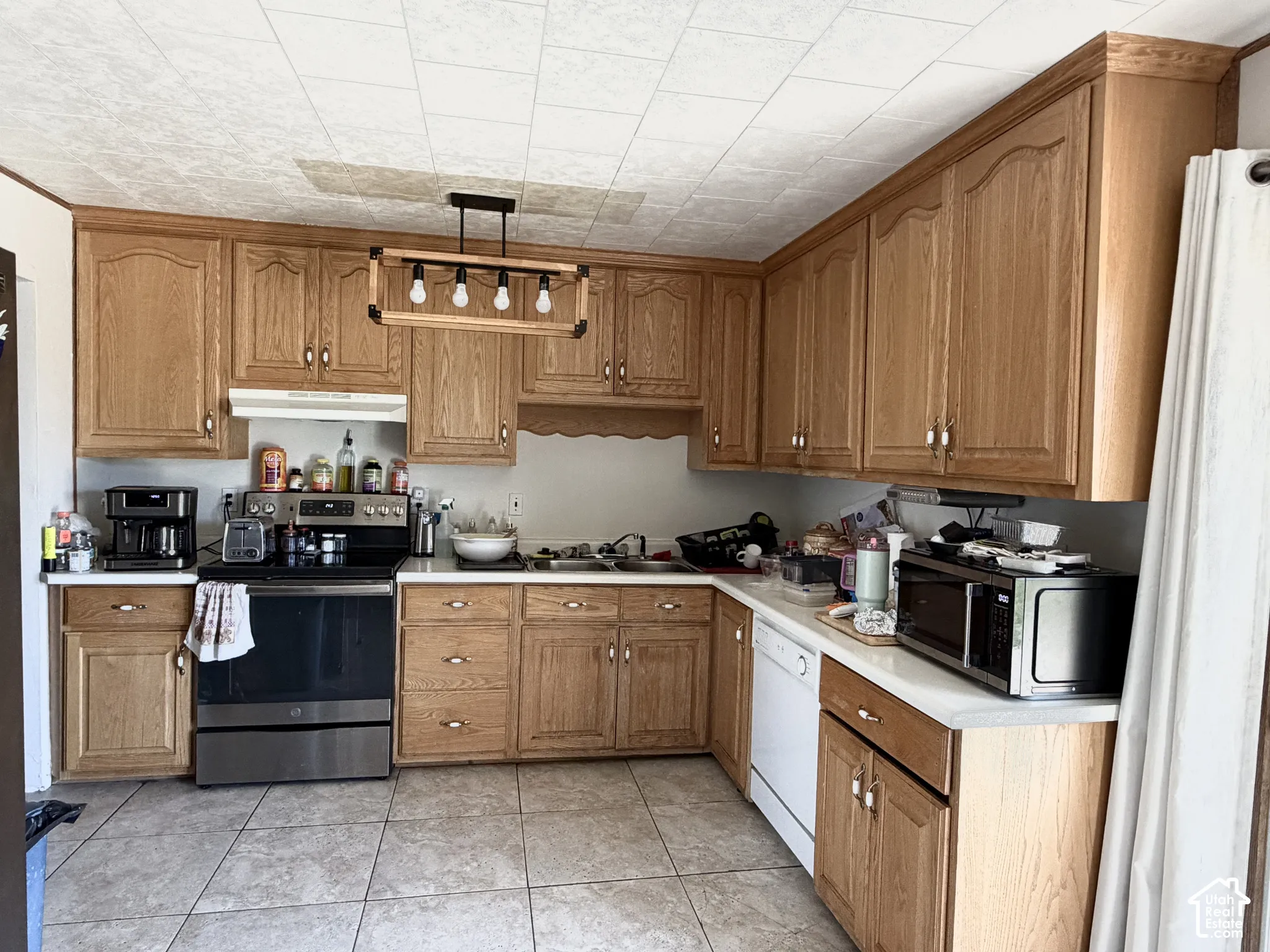 Kitchen featuring wood cabinetry, laminate countertops, a dual-basin stainless steel sink, tile flooring, and a linear pendant light fixture
