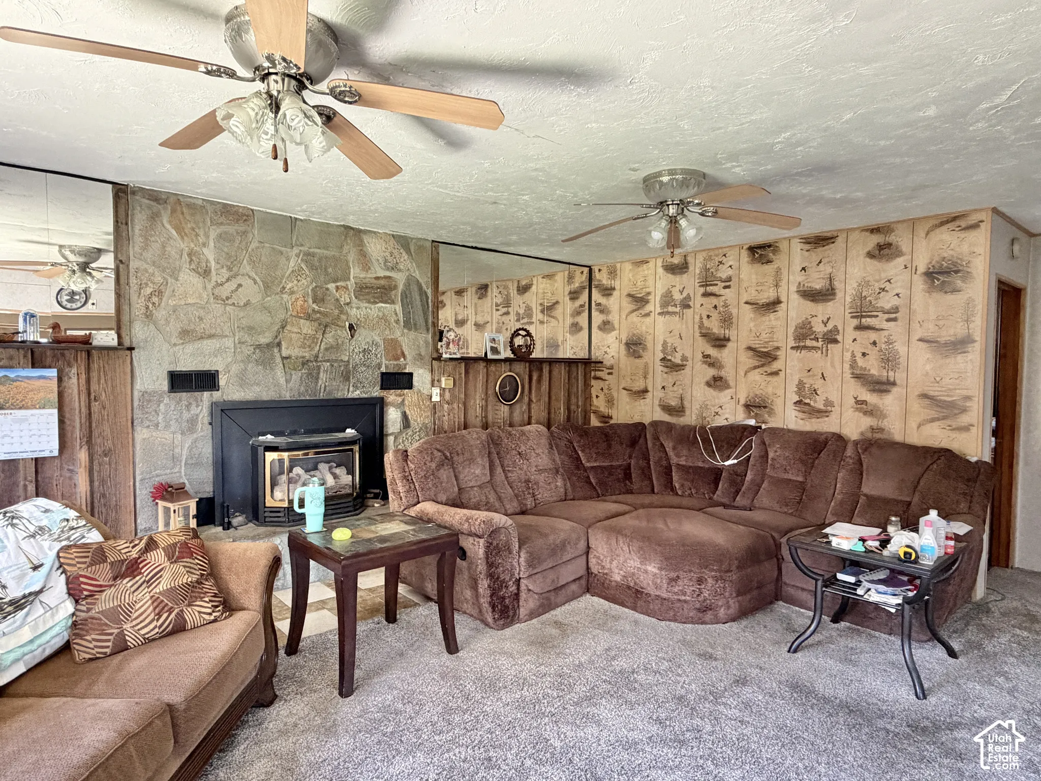 Floor-to-ceiling stone fireplace with an integrated stove insert, wood-paneled walls, mirrored wall accents, and dual ceiling fans