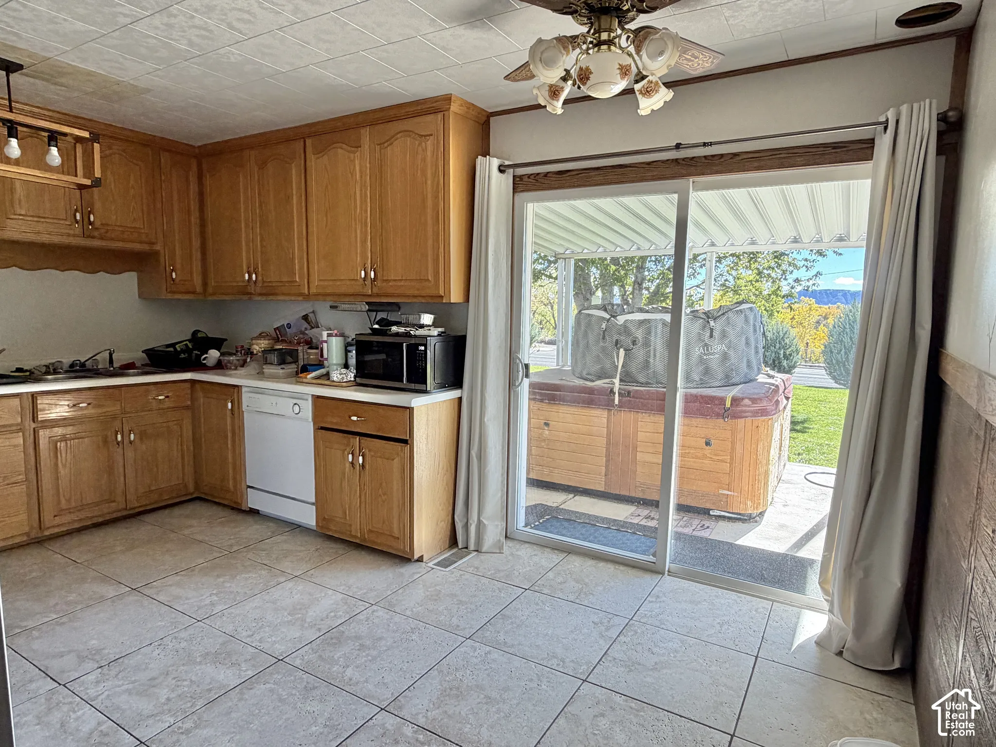 Kitchen featuring wood cabinetry, tile flooring, built-in dishwasher, and a sliding glass door opening to a covered patio