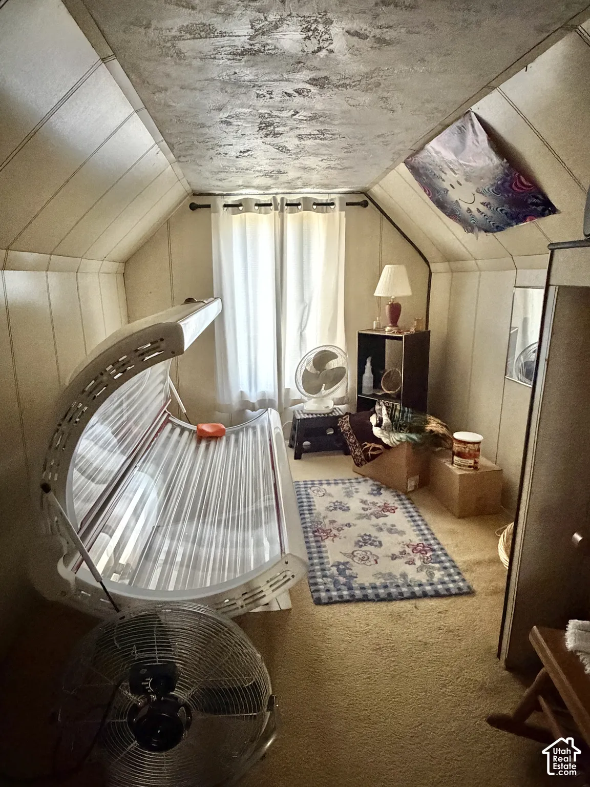 Vaulted ceiling with angled wall paneling, wall-to-wall carpeting, and a centered window with curtain hardware