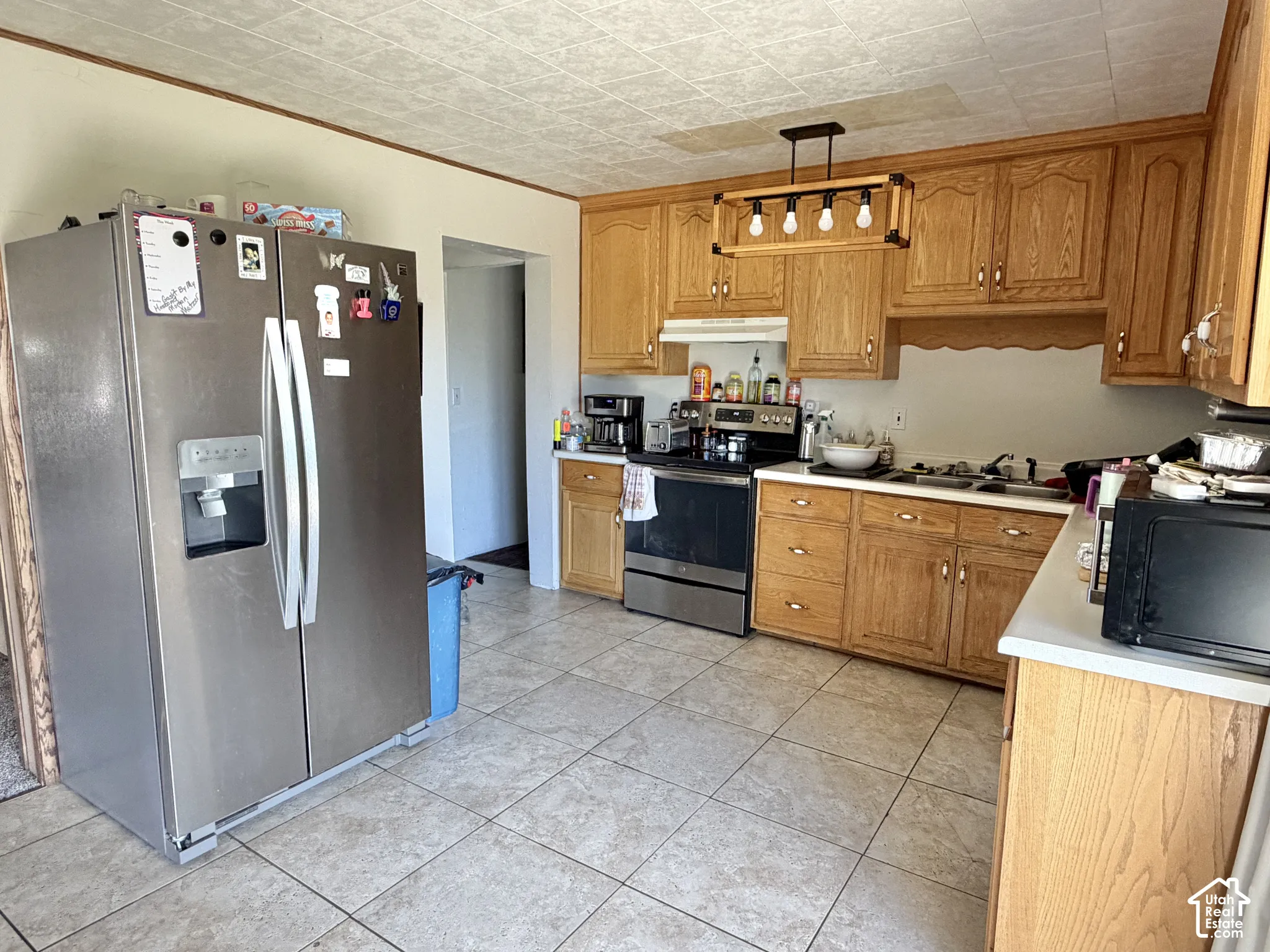 Kitchen featuring wood cabinetry, stainless steel appliances, tile flooring, and a linear pendant light fixture
