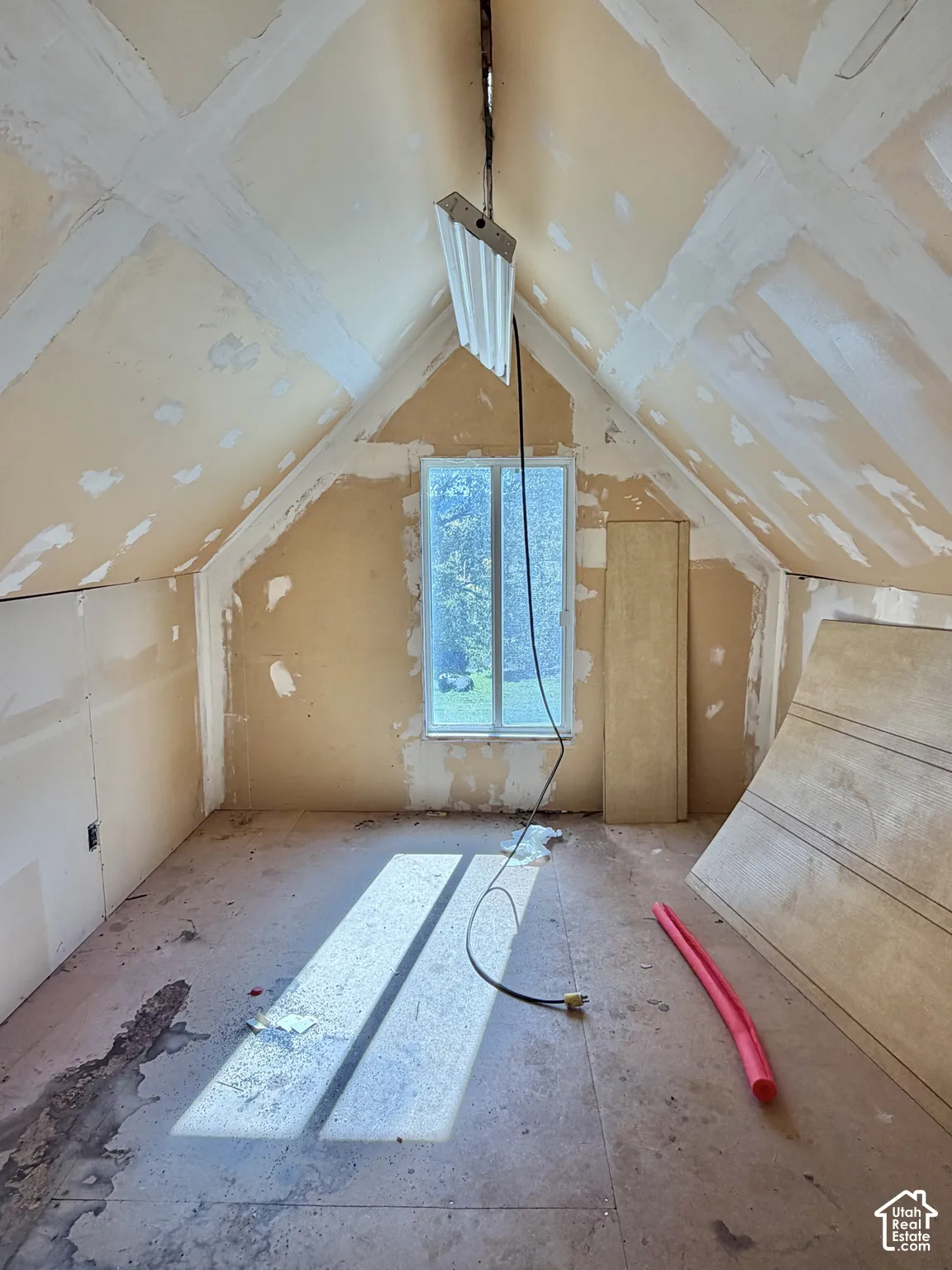 Attic space featuring vaulted ceilings, drywall paneling, and a single pane window