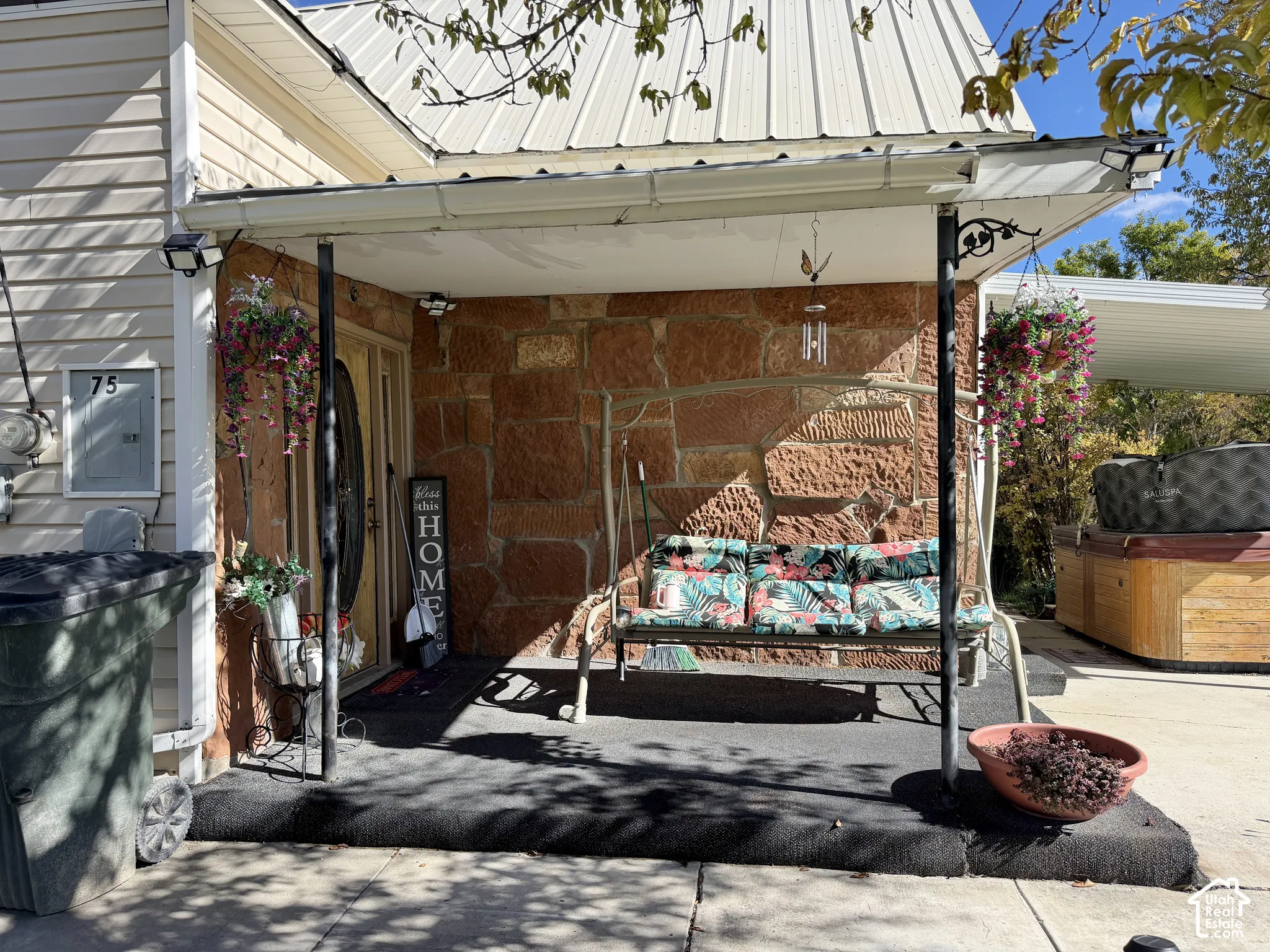 Covered porch featuring a natural stone accent wall, metal roofline, and support columns
