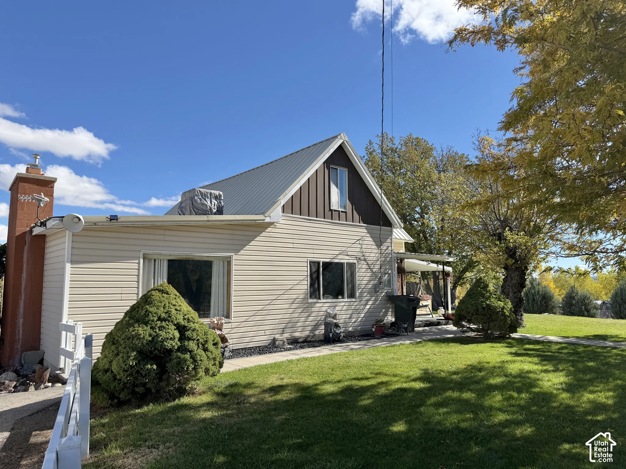 Exterior featuring light-colored horizontal siding, a steep-pitched metal roof, vertical gable siding, and an external masonry chimney