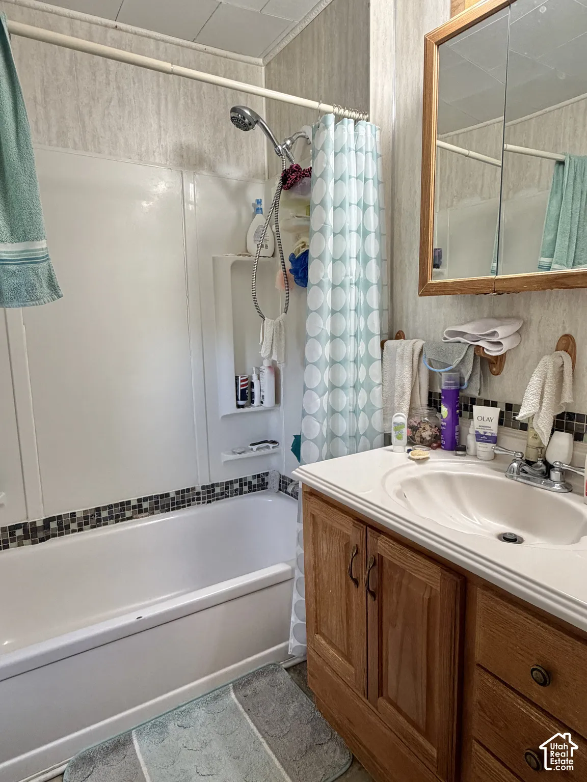Bathroom featuring a wood vanity with integrated countertop, inset sink, chrome faucet, and mirrored medicine cabinet, accompanied by a bathtub with a shower surround and decorative tile inlay
