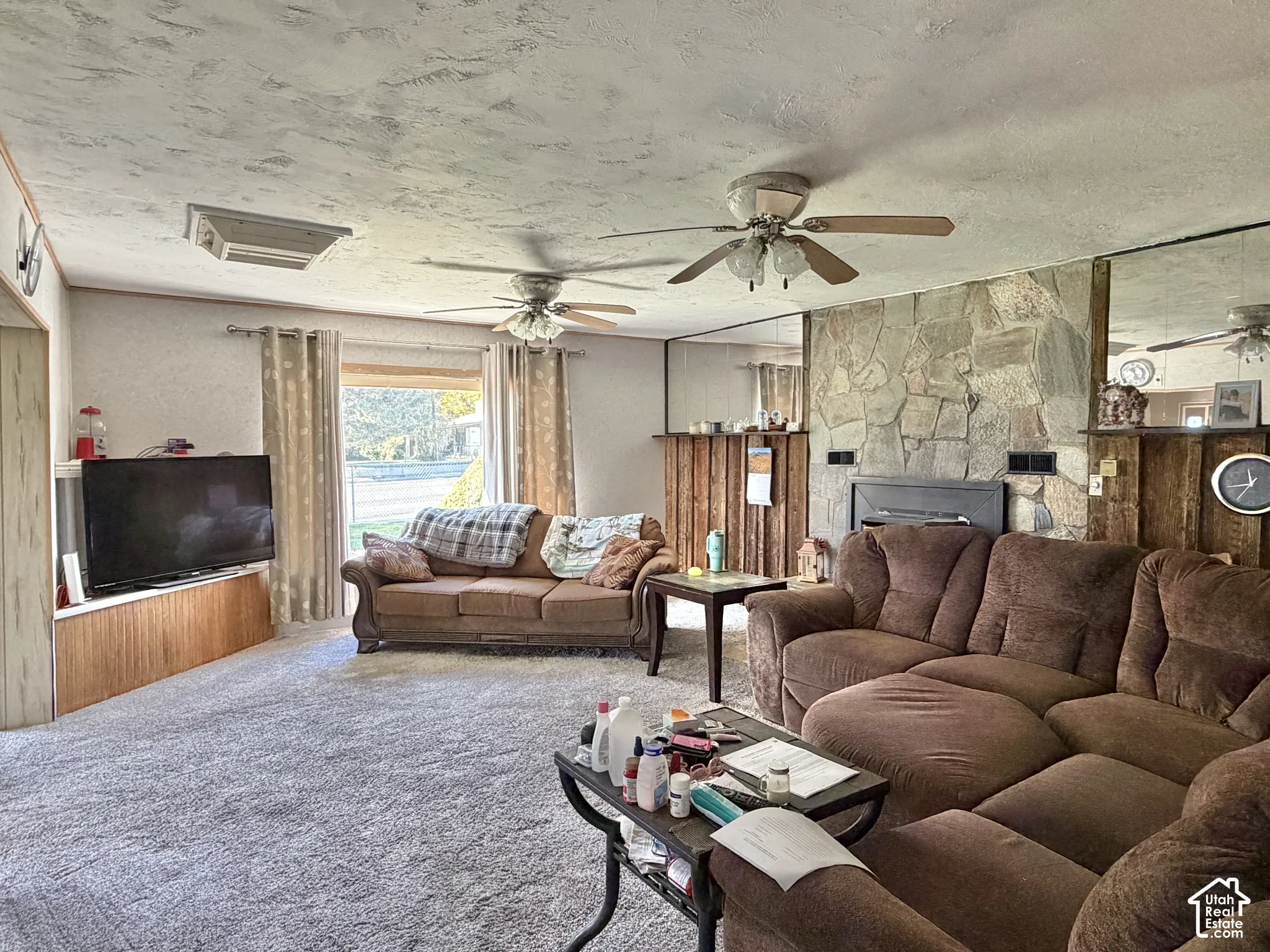 Living area featuring a floor-to-ceiling stone accent wall with a built-in fireplace, dual ceiling fans, mirrored wall panels, and wood-finish cabinetry