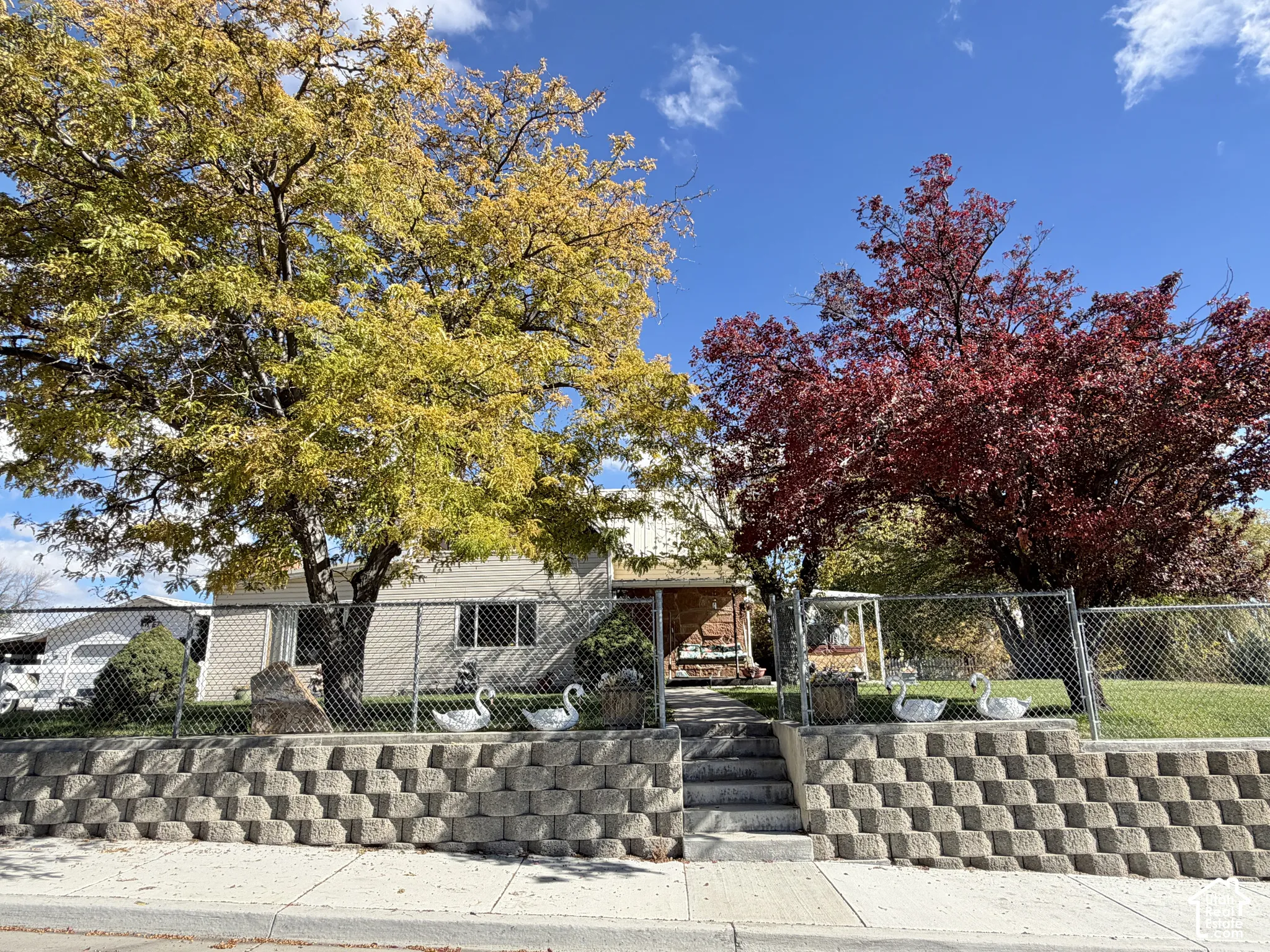 Tiered stone retaining wall with concrete steps, chain-link fencing, and mature deciduous trees