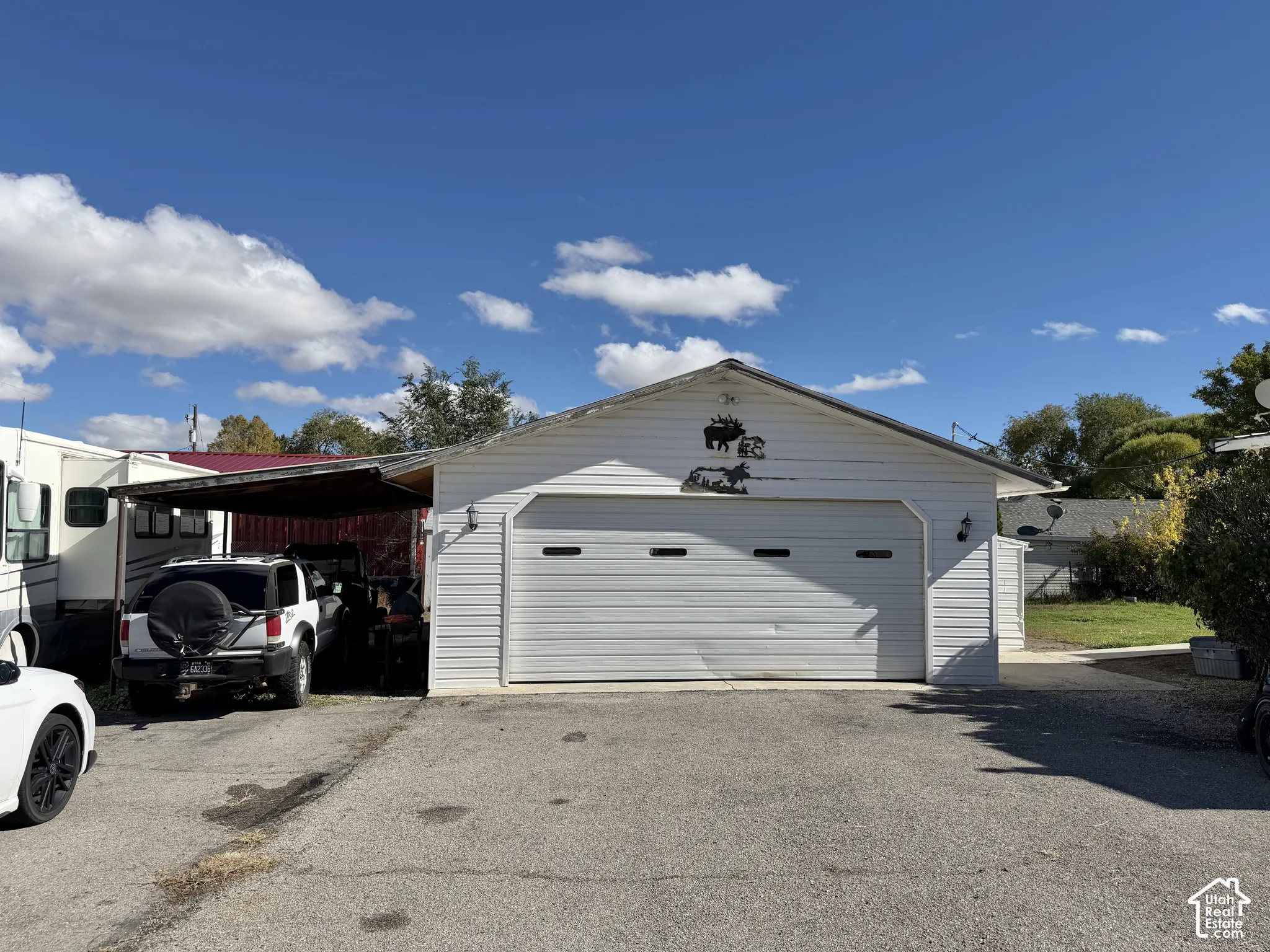 Detached garage featuring white horizontal siding, a paved driveway, and an attached metal-frame carport